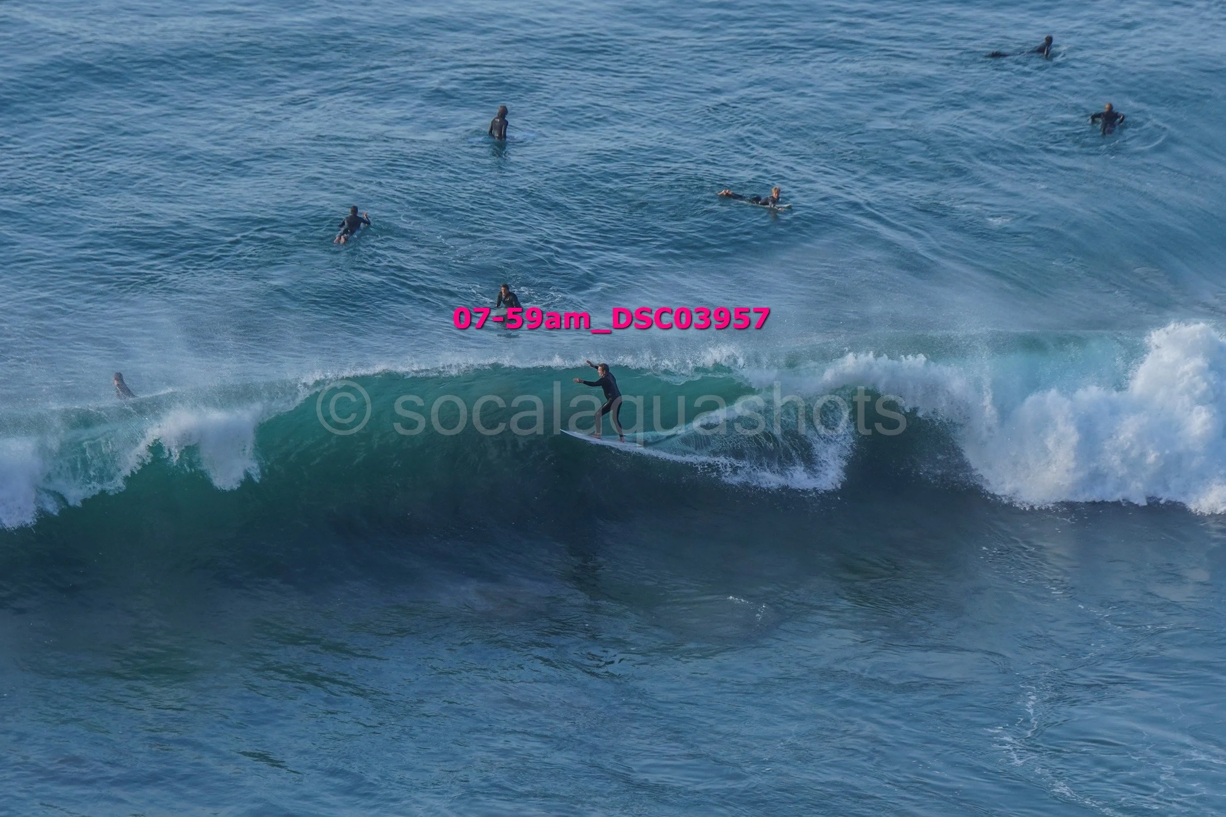 Surfer riding a wave with multiple surfers in the water in the background.