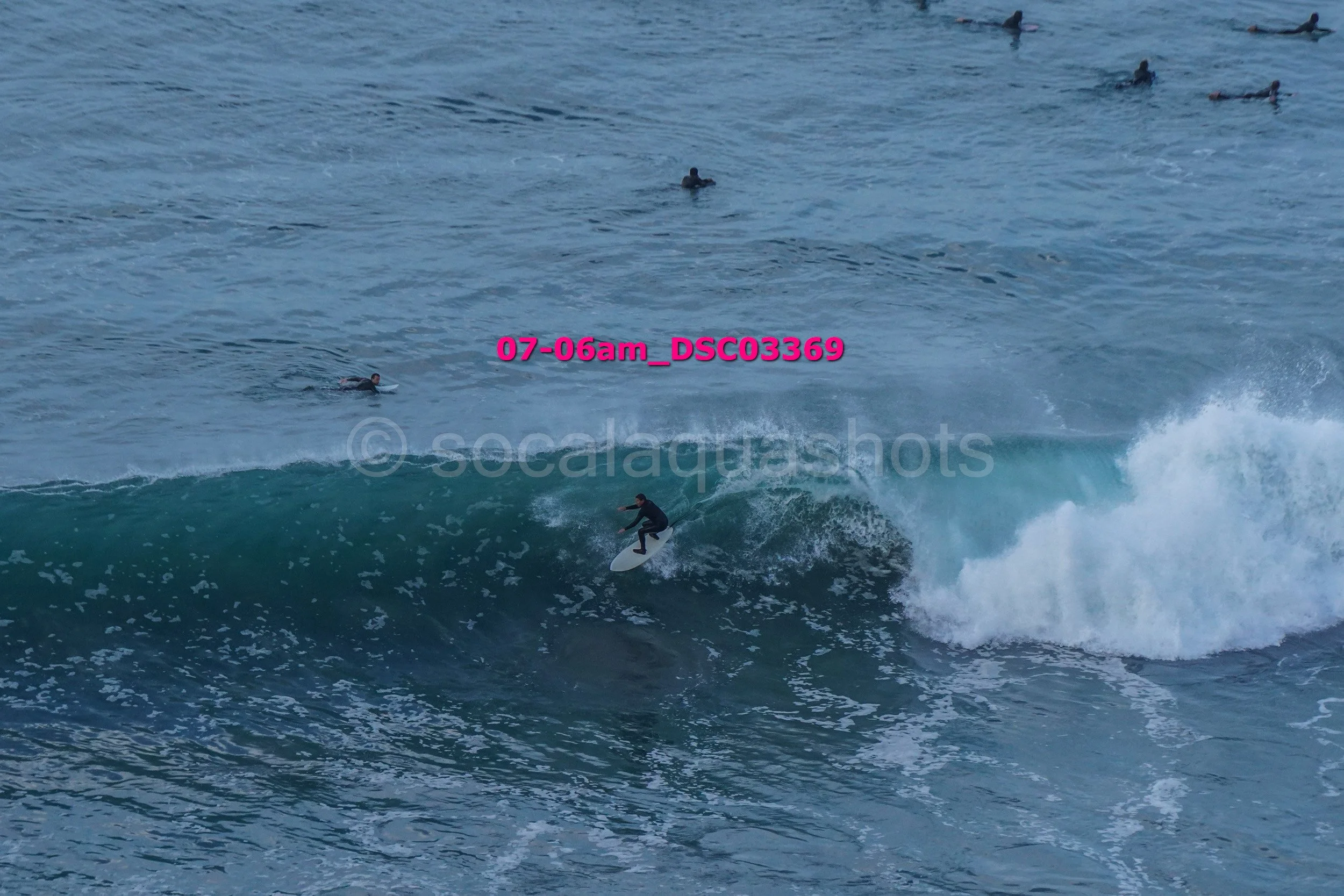 Surfer riding a wave with several people in the water in the background.