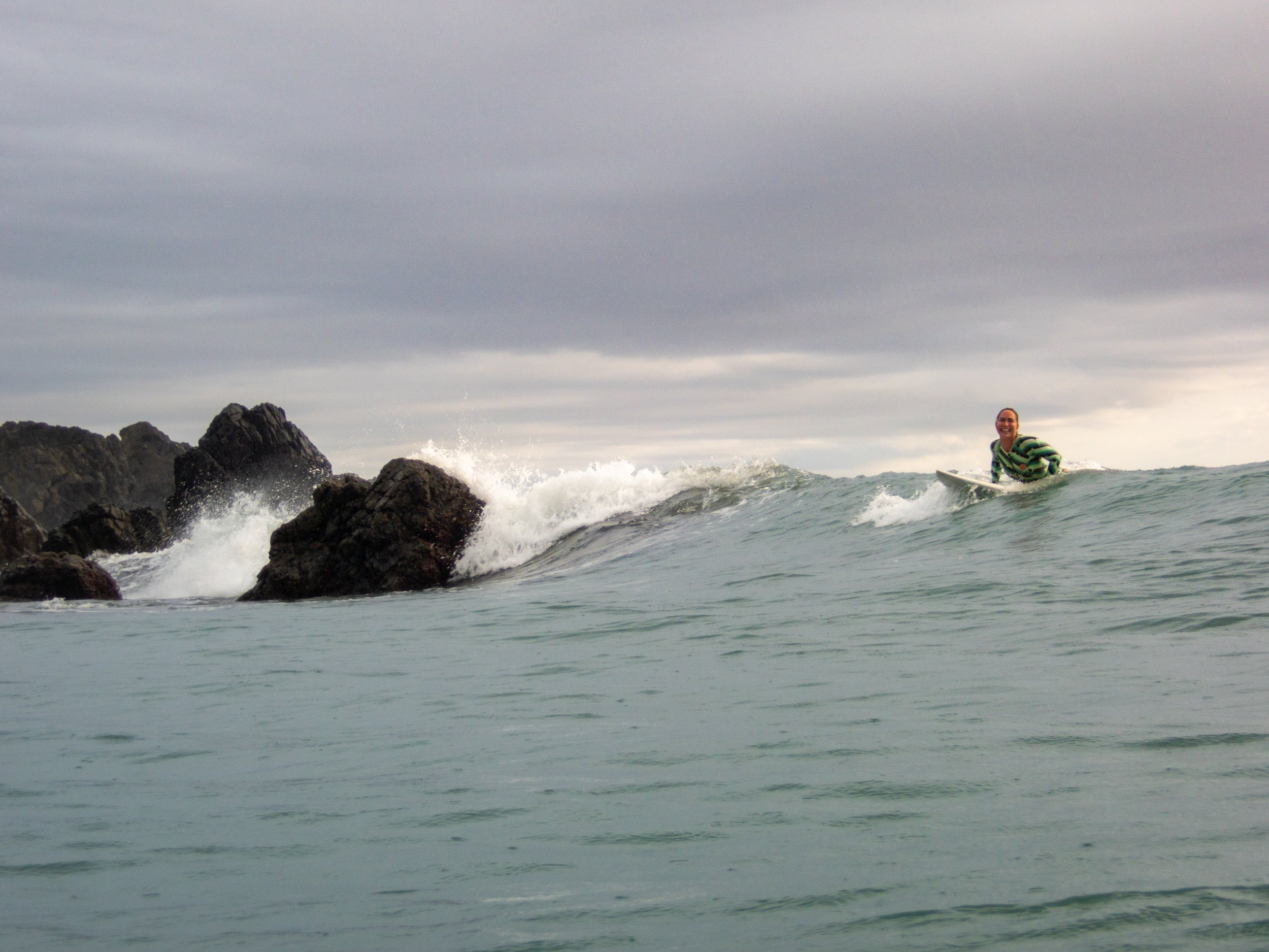 Surfer riding a wave near rocky coastline under a cloudy sky