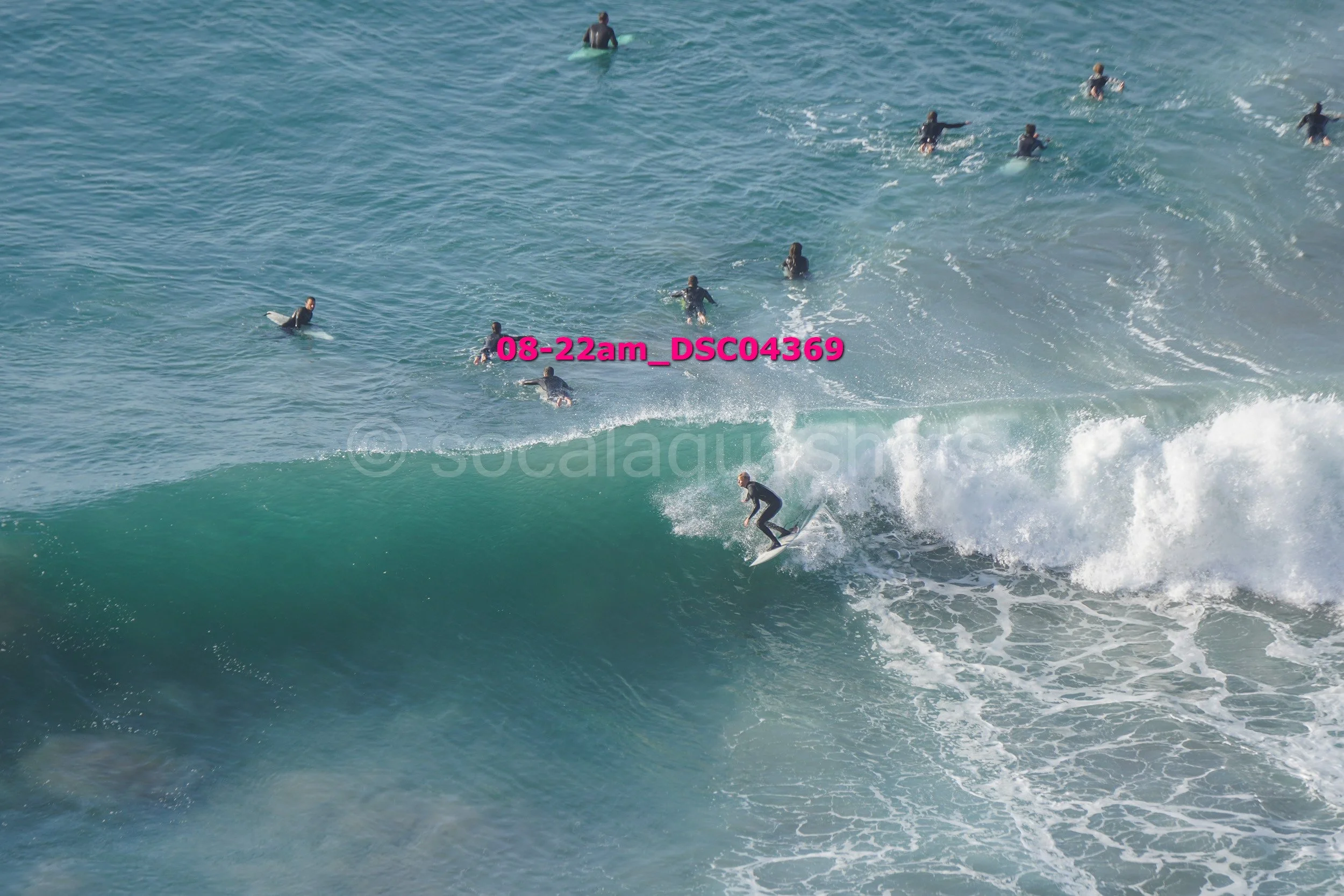 Surfer riding a wave with multiple surfers in the ocean behind him.