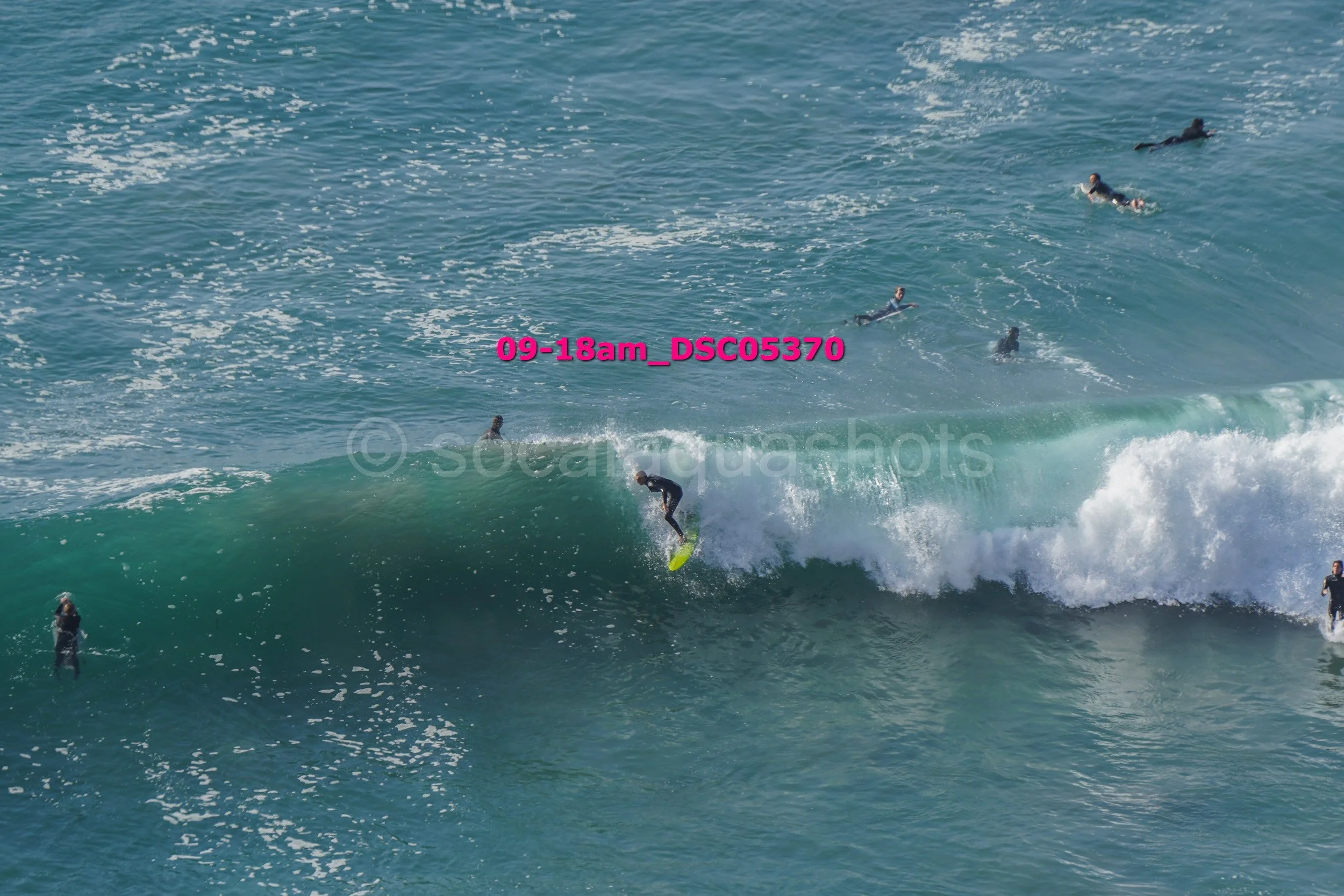 A person surfing on a wave with several surfers in the water around them.