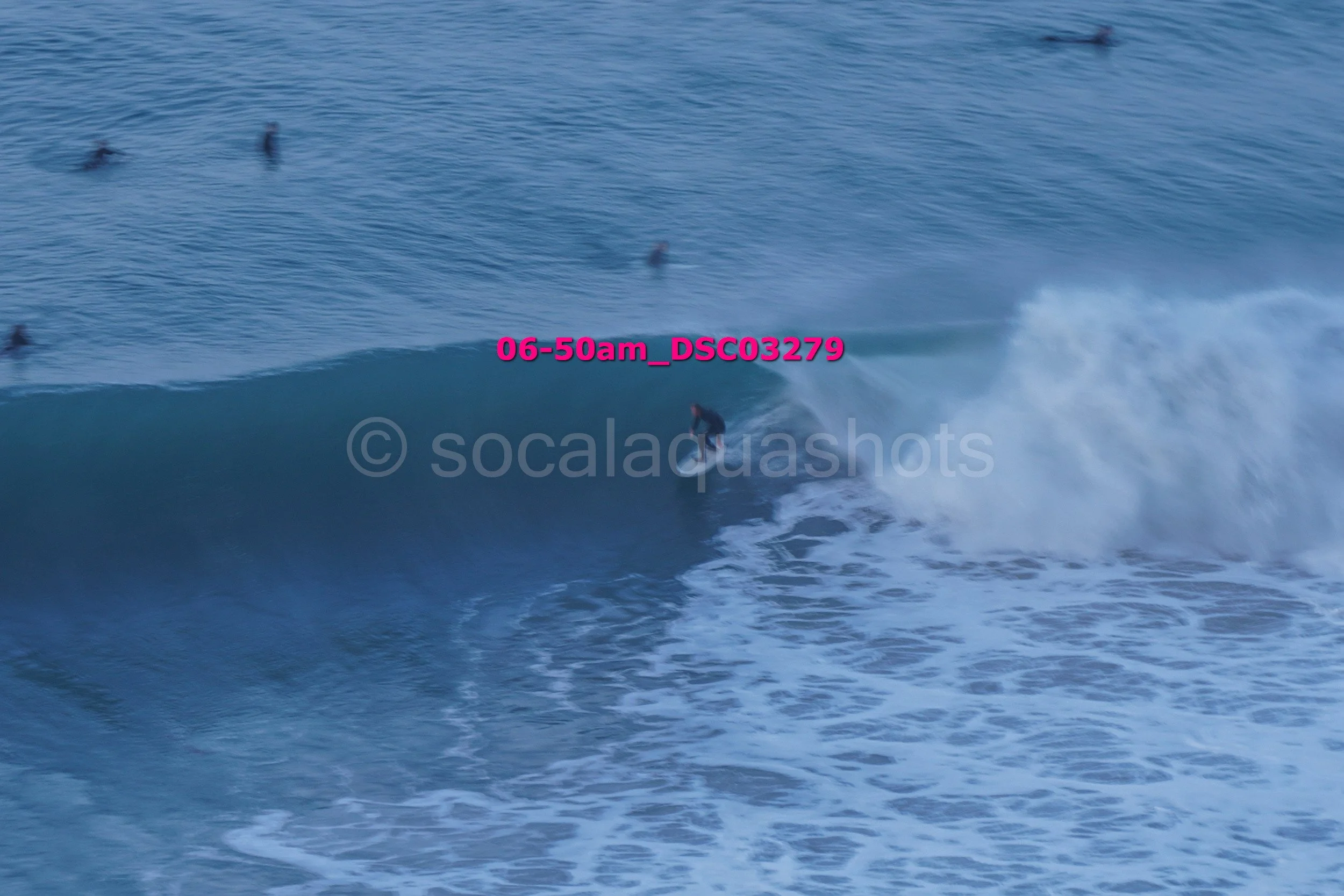 A person surfing on a wave in the ocean, with several surfers floating in the water nearby.
