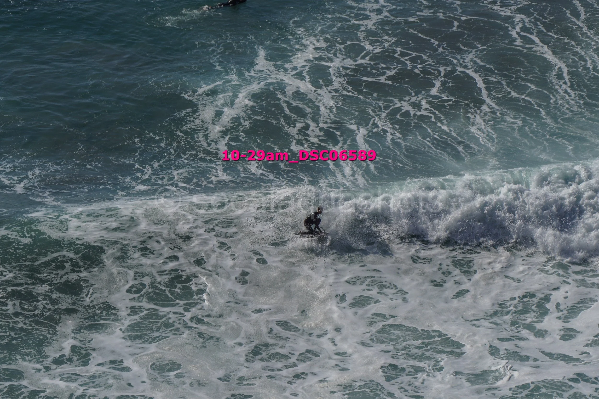A person surfing on a wave in the ocean with white foam and water currents visible.