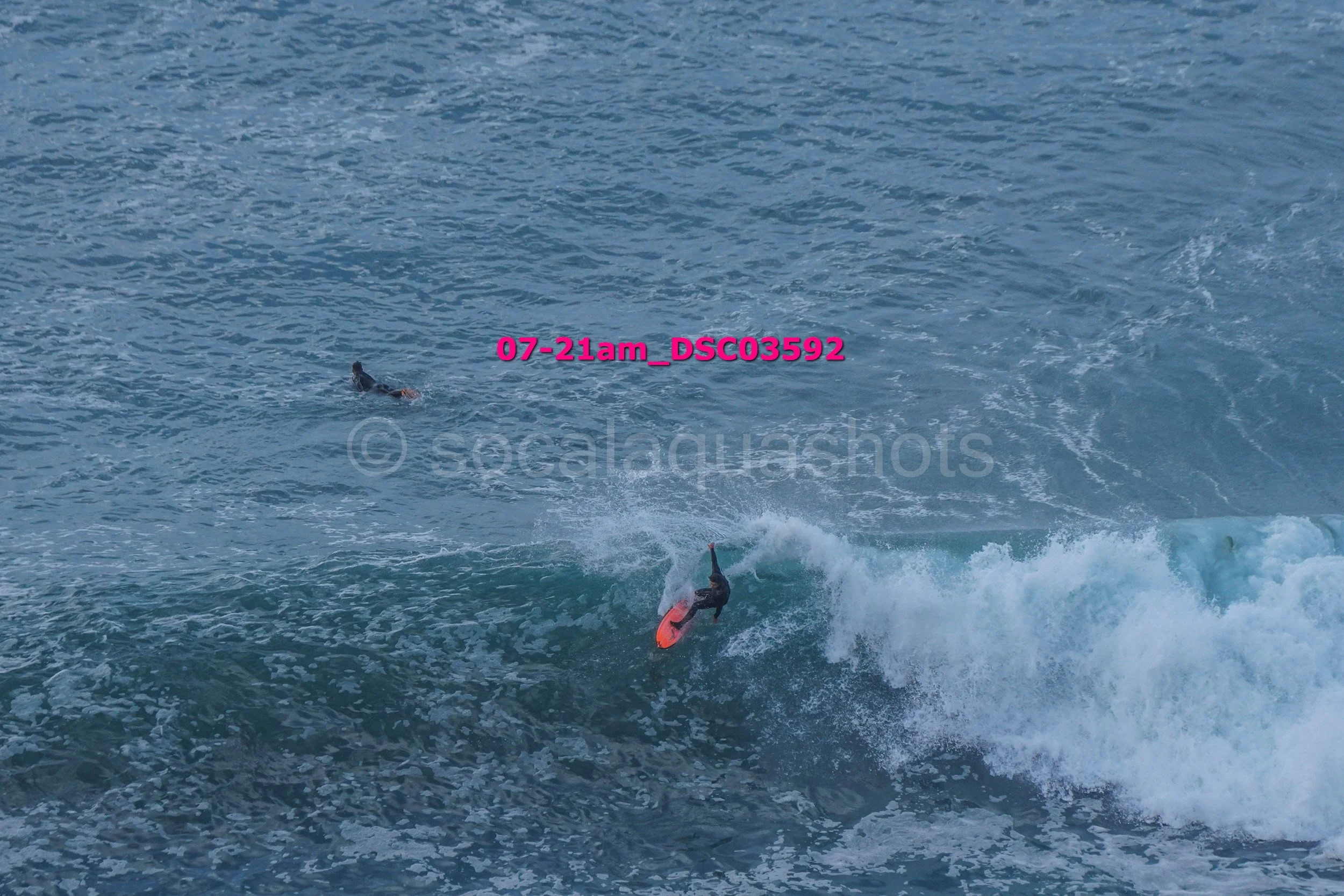 A person surfing on a wave in the ocean, with another individual swimming nearby in the water.