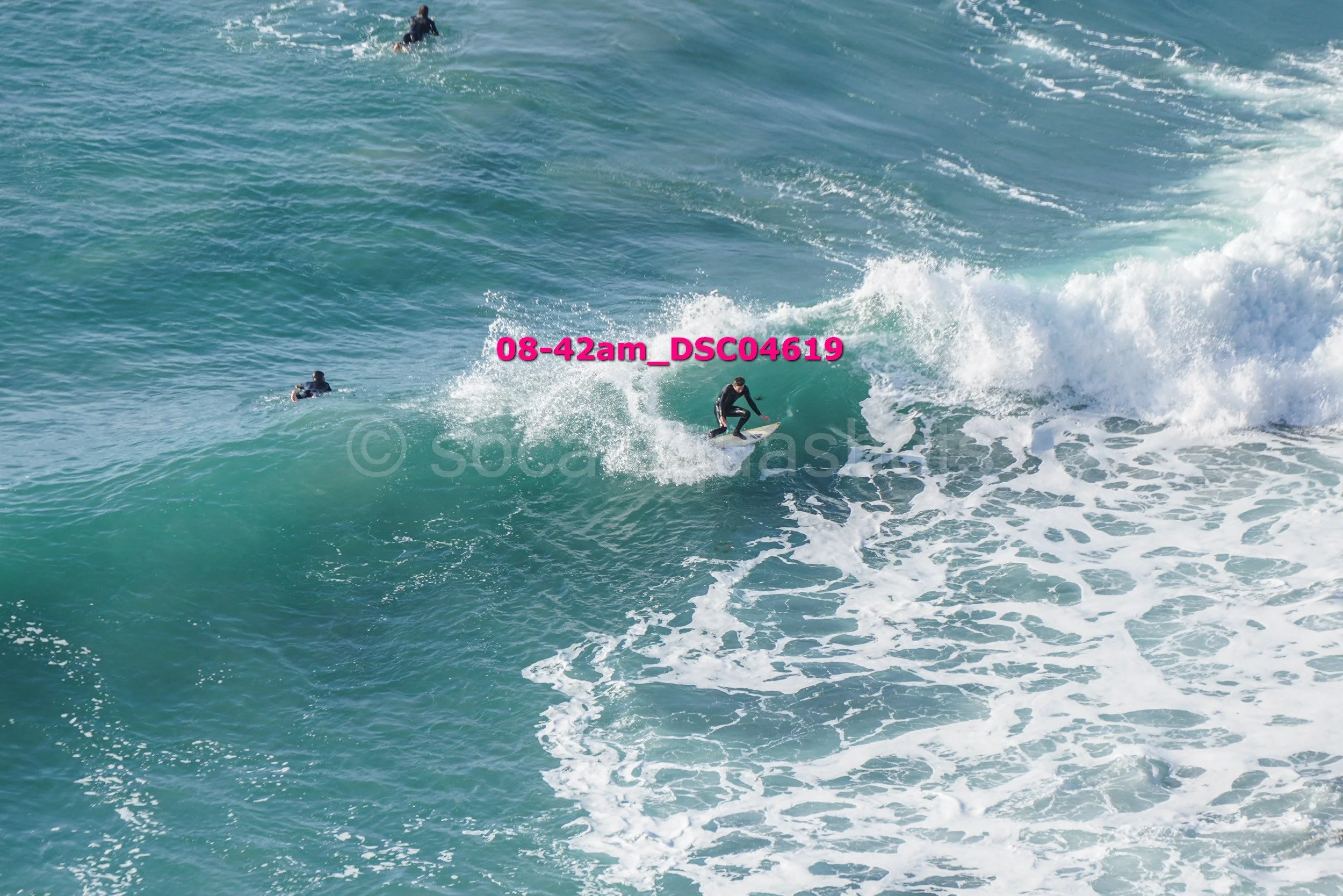 Surfer riding a wave in the ocean with two other surfers nearby in the water.