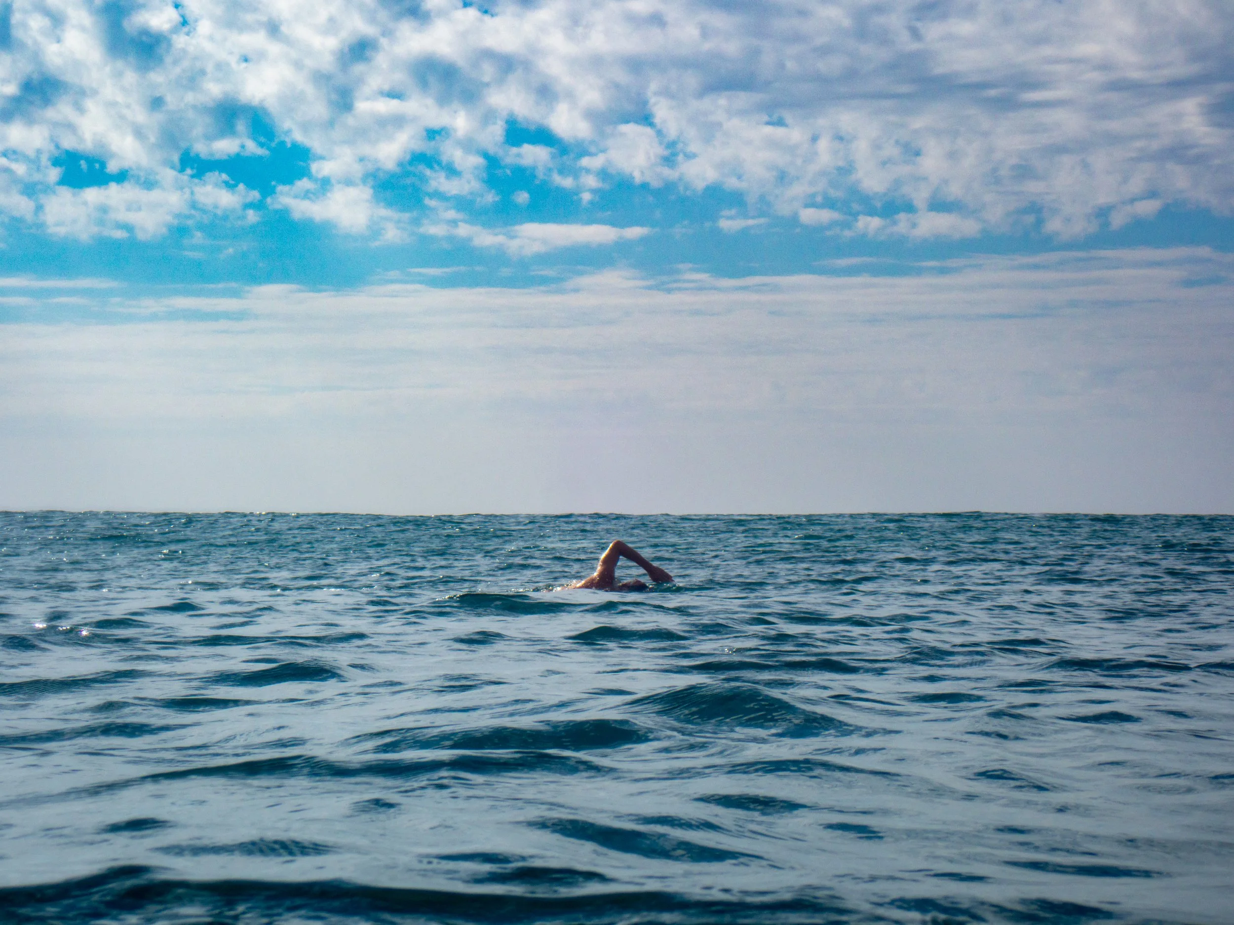 A person swimming in the ocean under a partly cloudy sky.