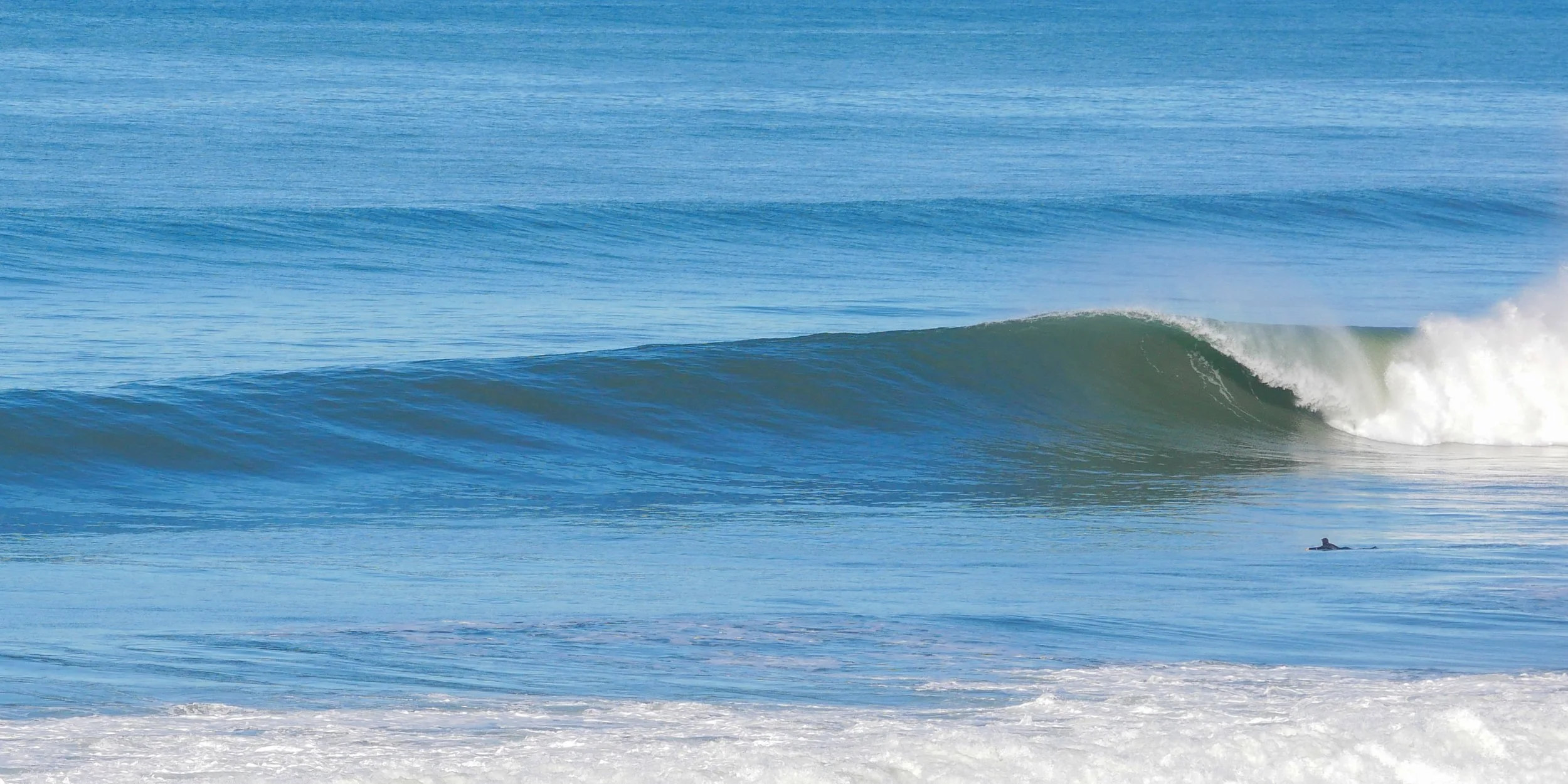 Ocean wave with surfer paddling in the foreground