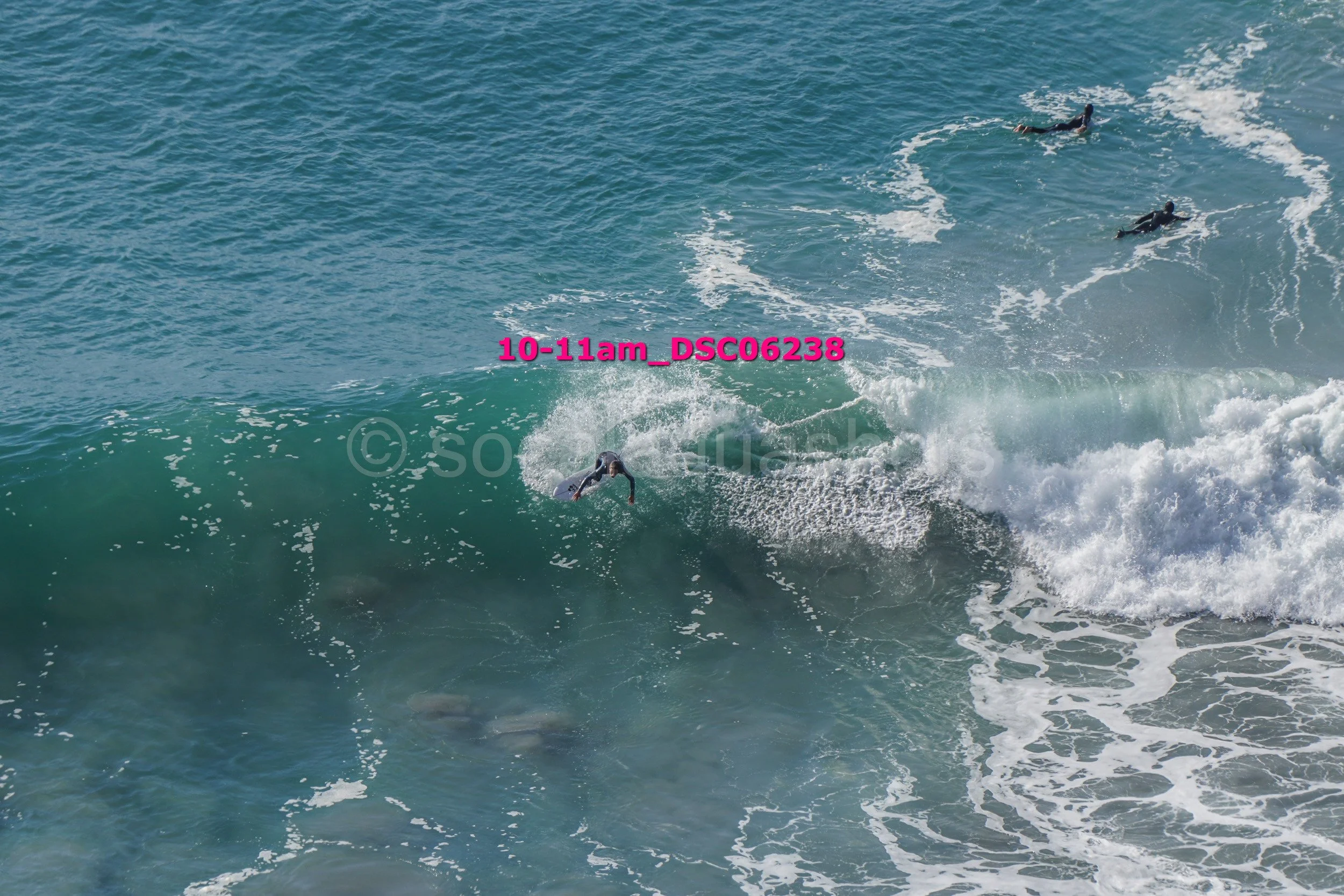 Surfer riding a wave with three other surfers visible in the distance in the ocean.