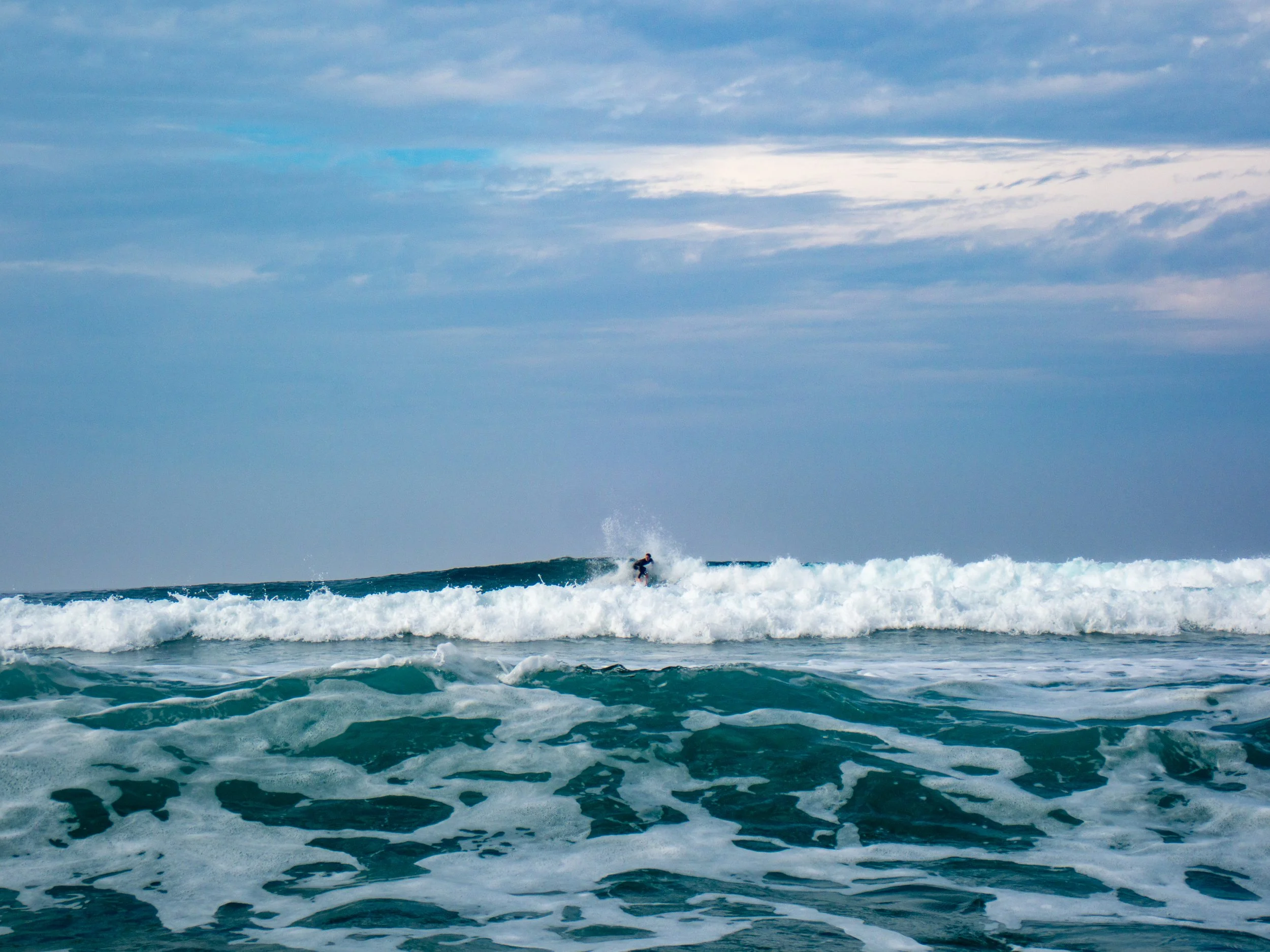 A surfer riding a wave in the ocean on a cloudy day.