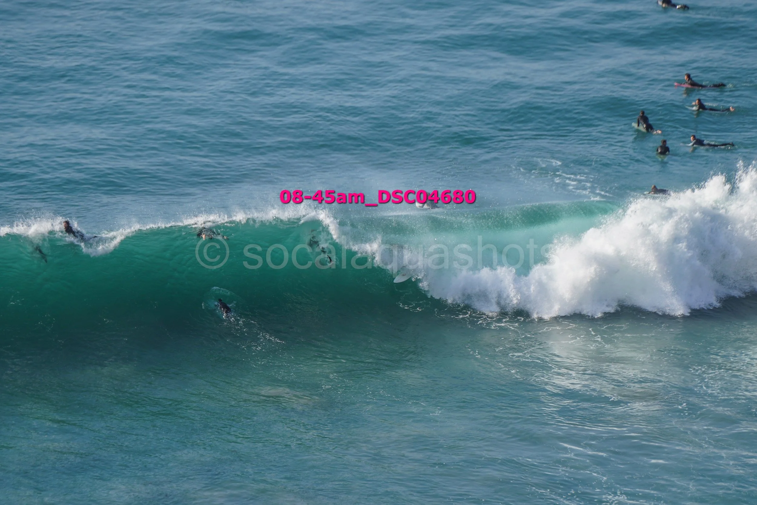 Surfers paddling and riding waves in the ocean, with some surfers on the water and others waiting on surfboards for waves to ride.