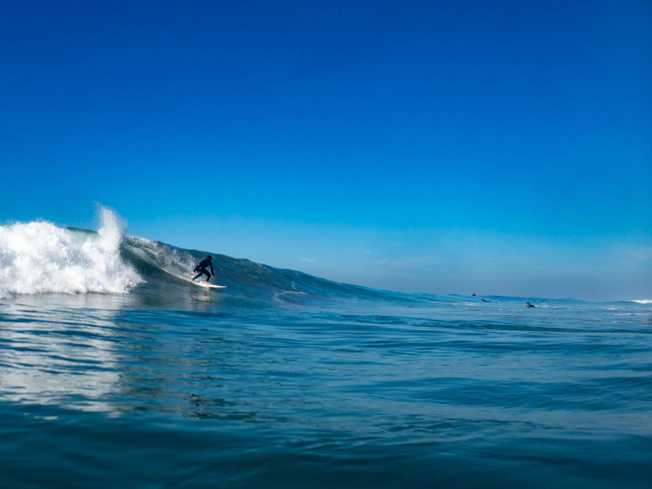A person surfing on a wave in the ocean on a clear, sunny day with a blue sky.