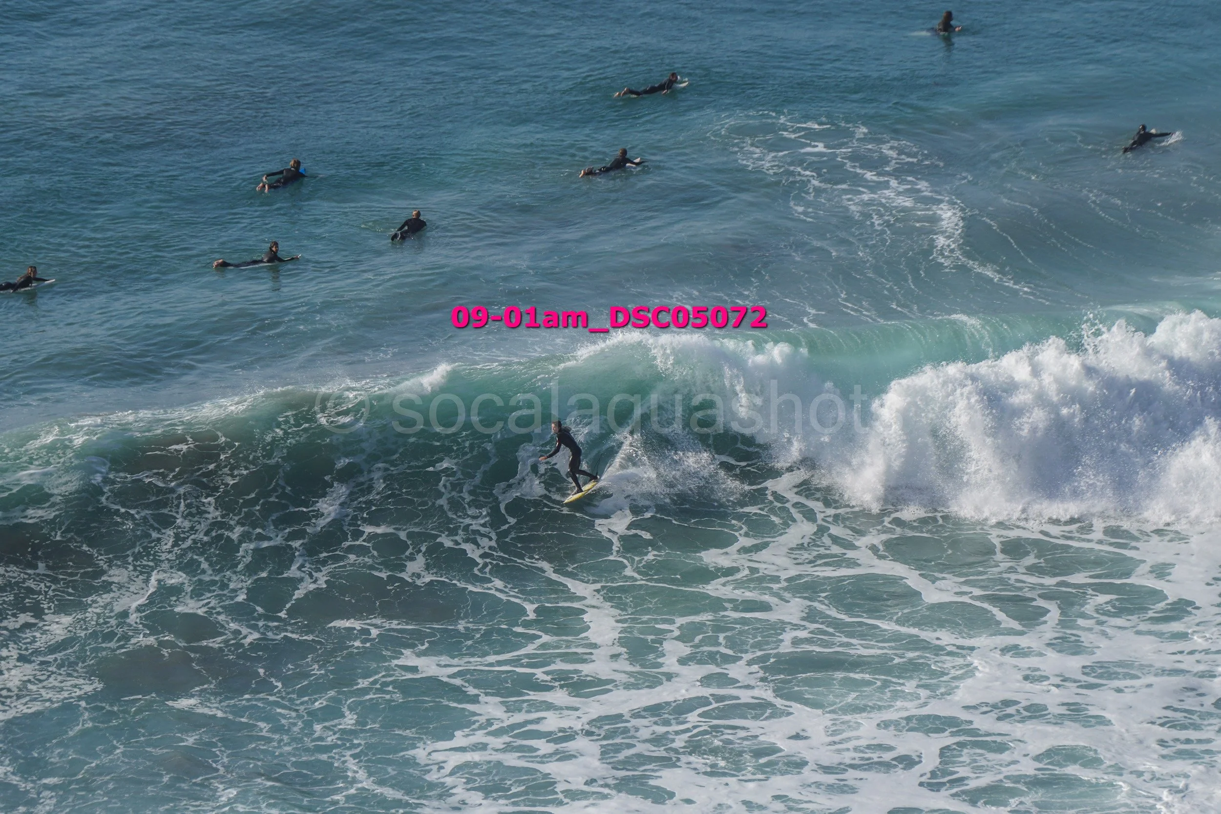 Surfer riding a wave with several other surfers in the water nearby.