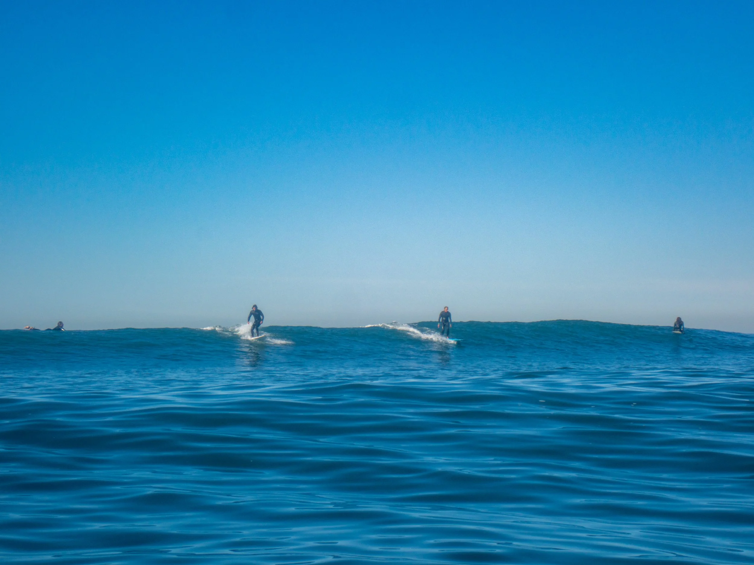 Several surfers riding small waves under a clear blue sky in the ocean.