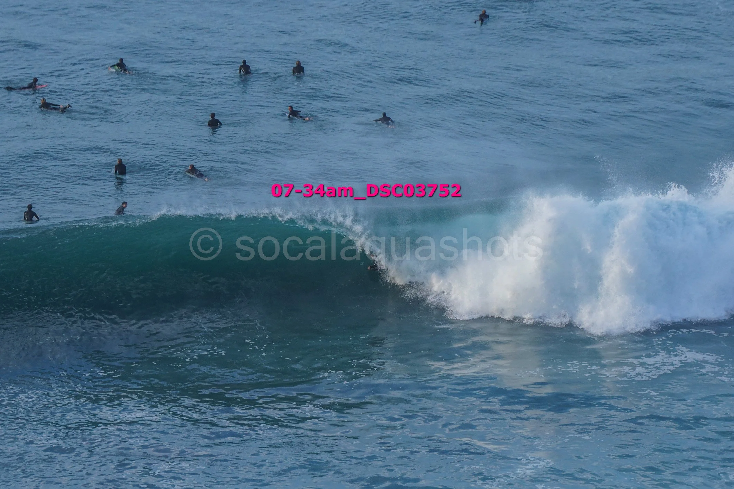 A group of surfers in wetsuits waiting in the water, with one surfer riding a wave close to the shore.