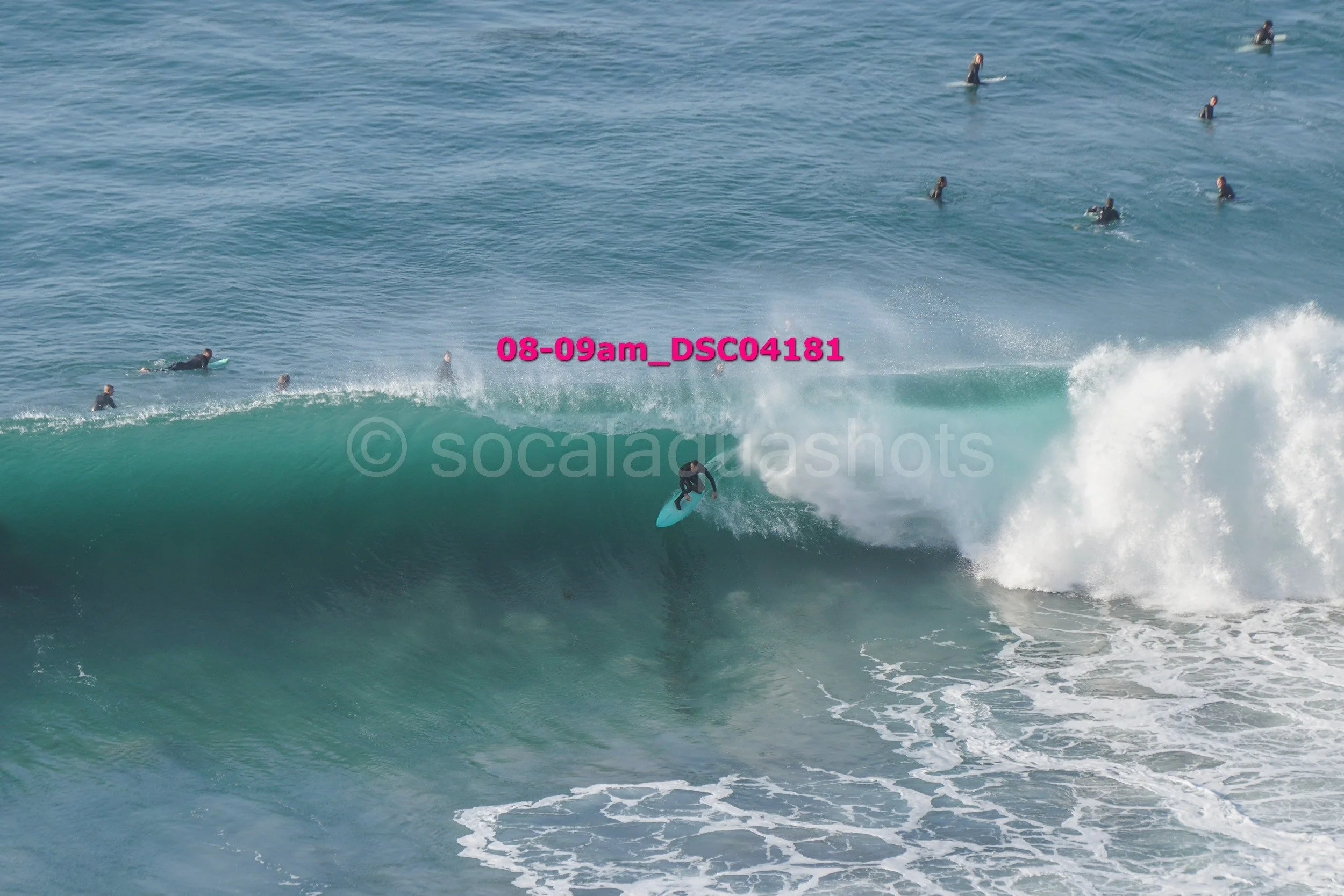 A surfer riding a large wave with smaller waves and multiple surfers in the water in the background