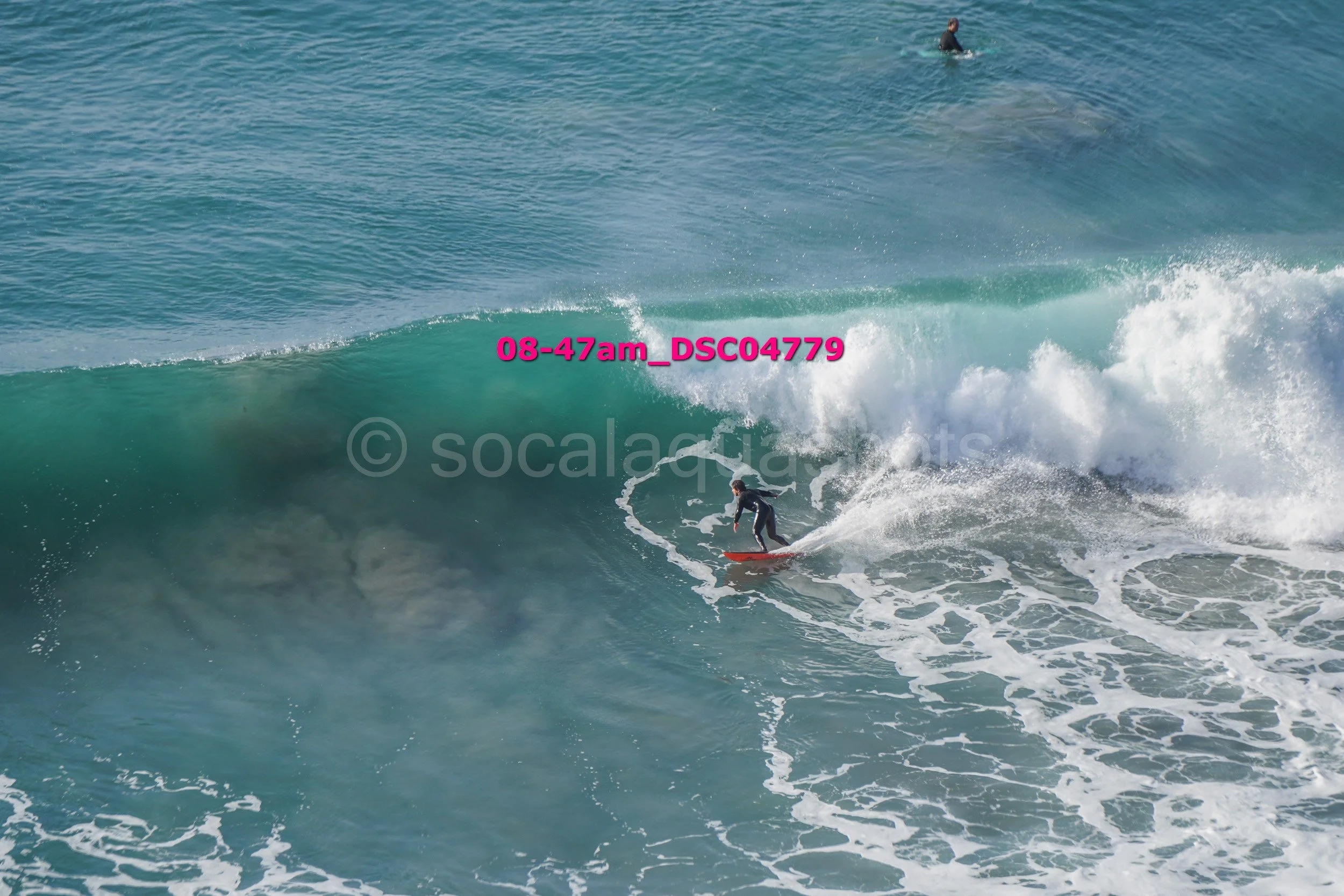 A person surfing on a large ocean wave, with another surfer in the background, in the water.