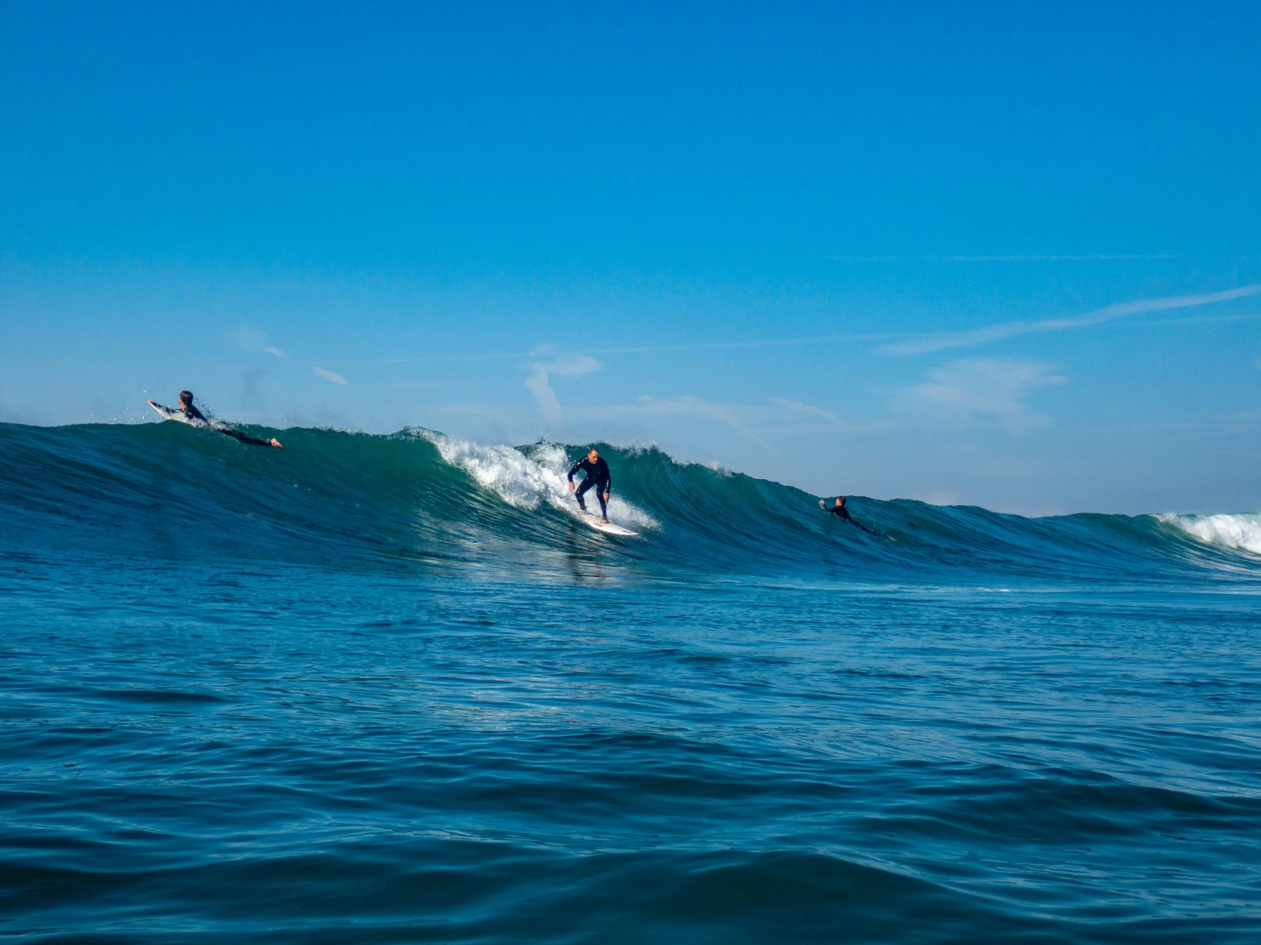 Three surfers riding waves in the ocean under a clear blue sky.