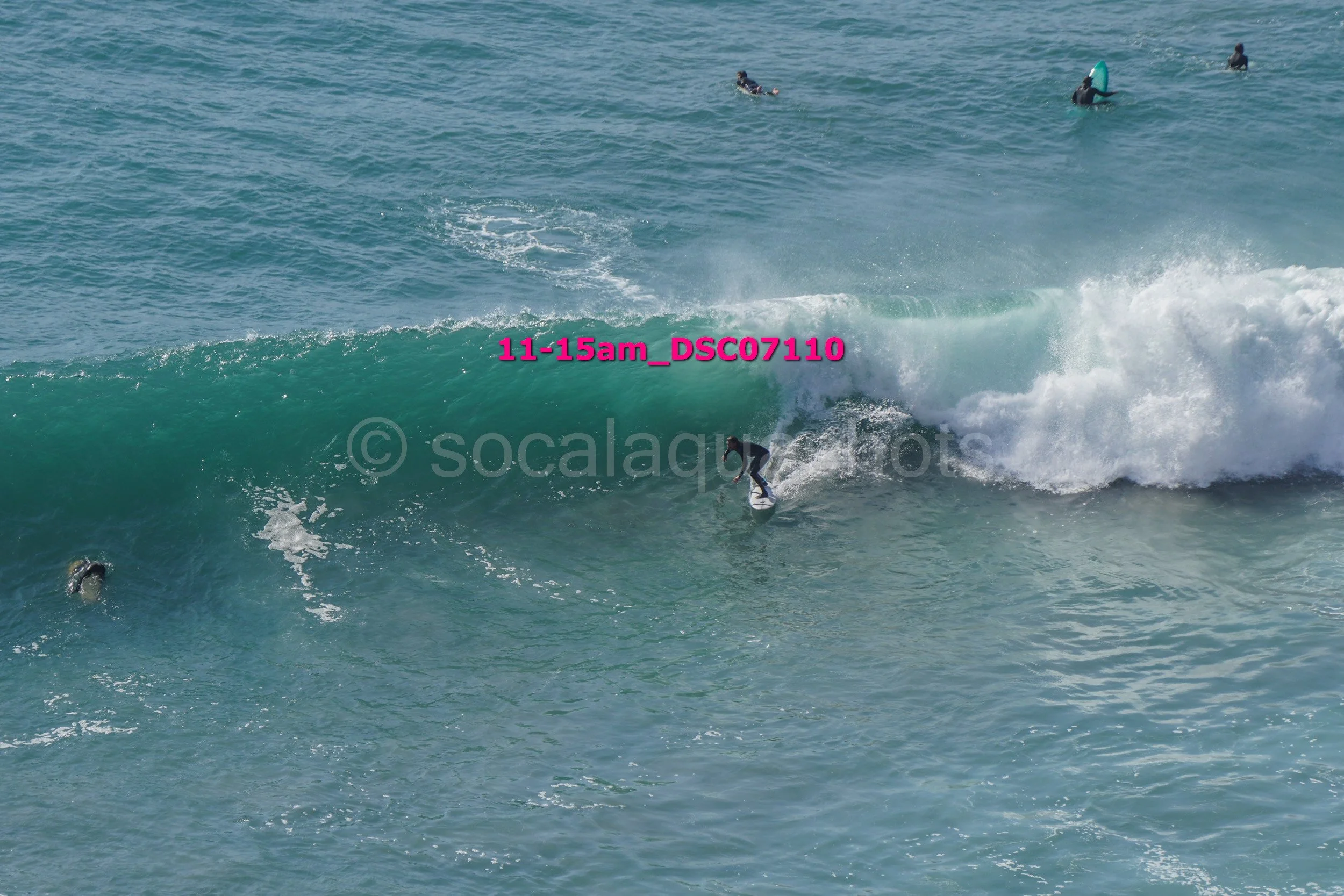 A group of surfers in the ocean, with one surfer riding a wave while others wait in the water.