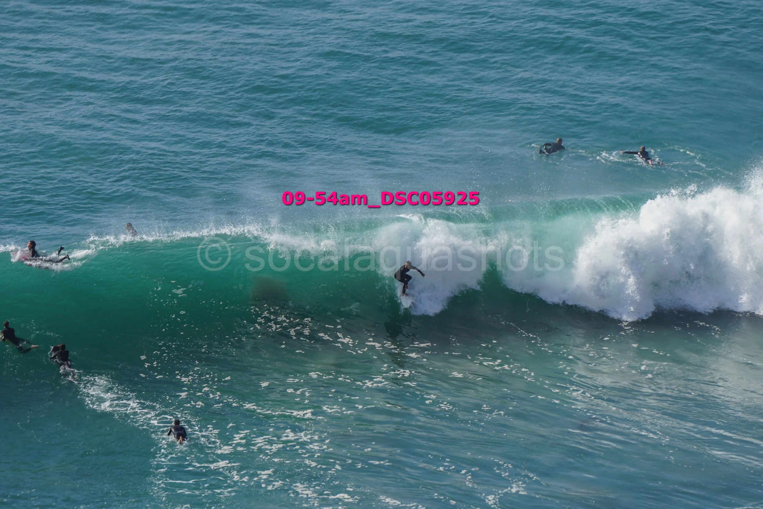 Surfer riding a wave with several other surfers in the water.