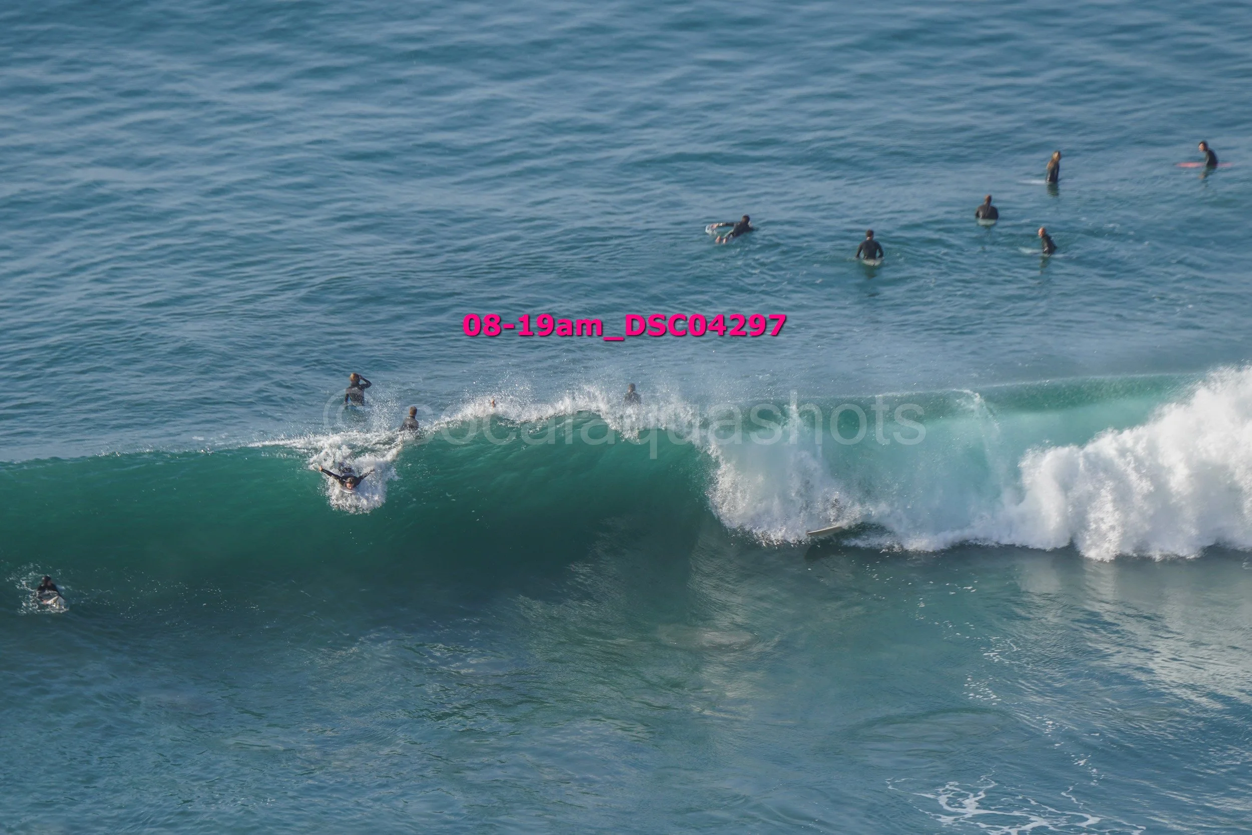 Surfer riding a wave with several people swimming and surfing in the water nearby.