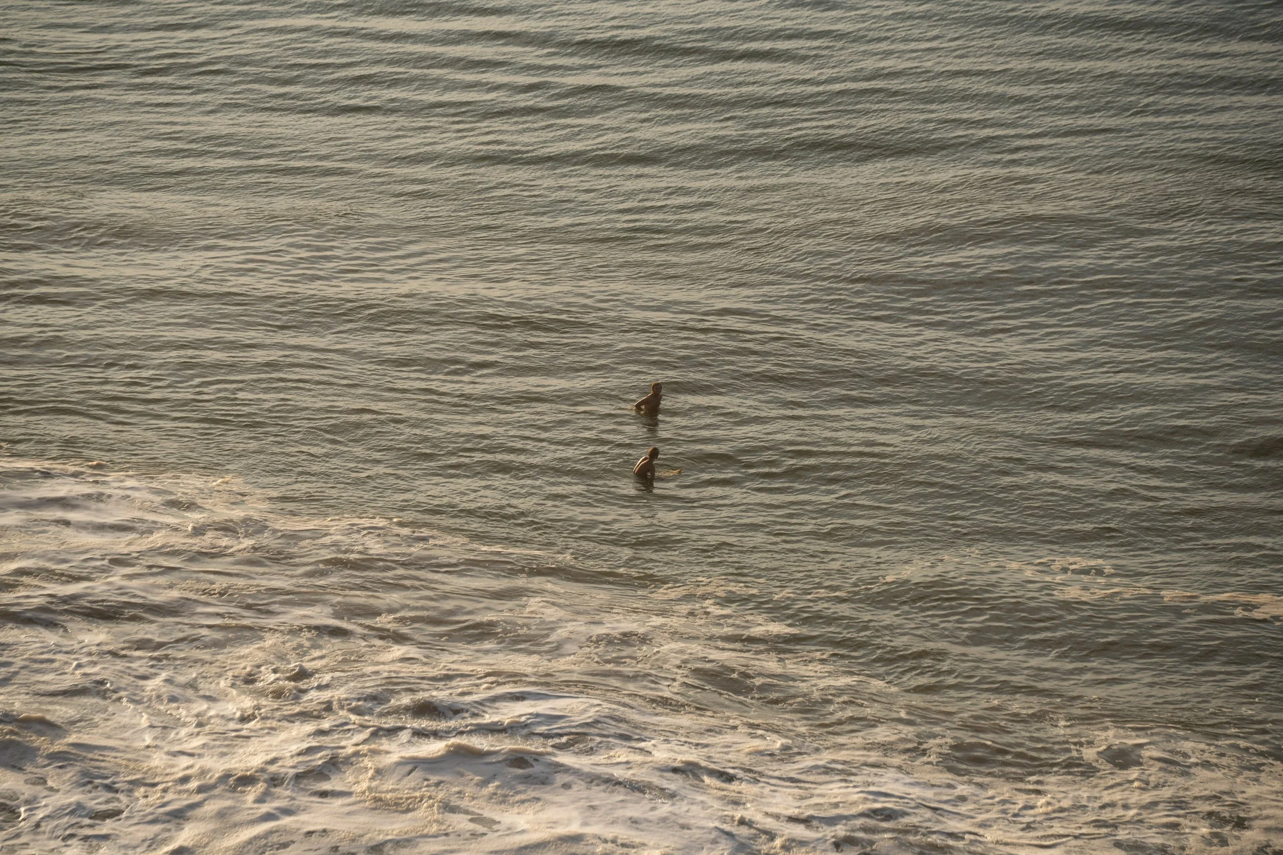 Two children swimming in the ocean with gentle waves and a warm, golden sunset.
