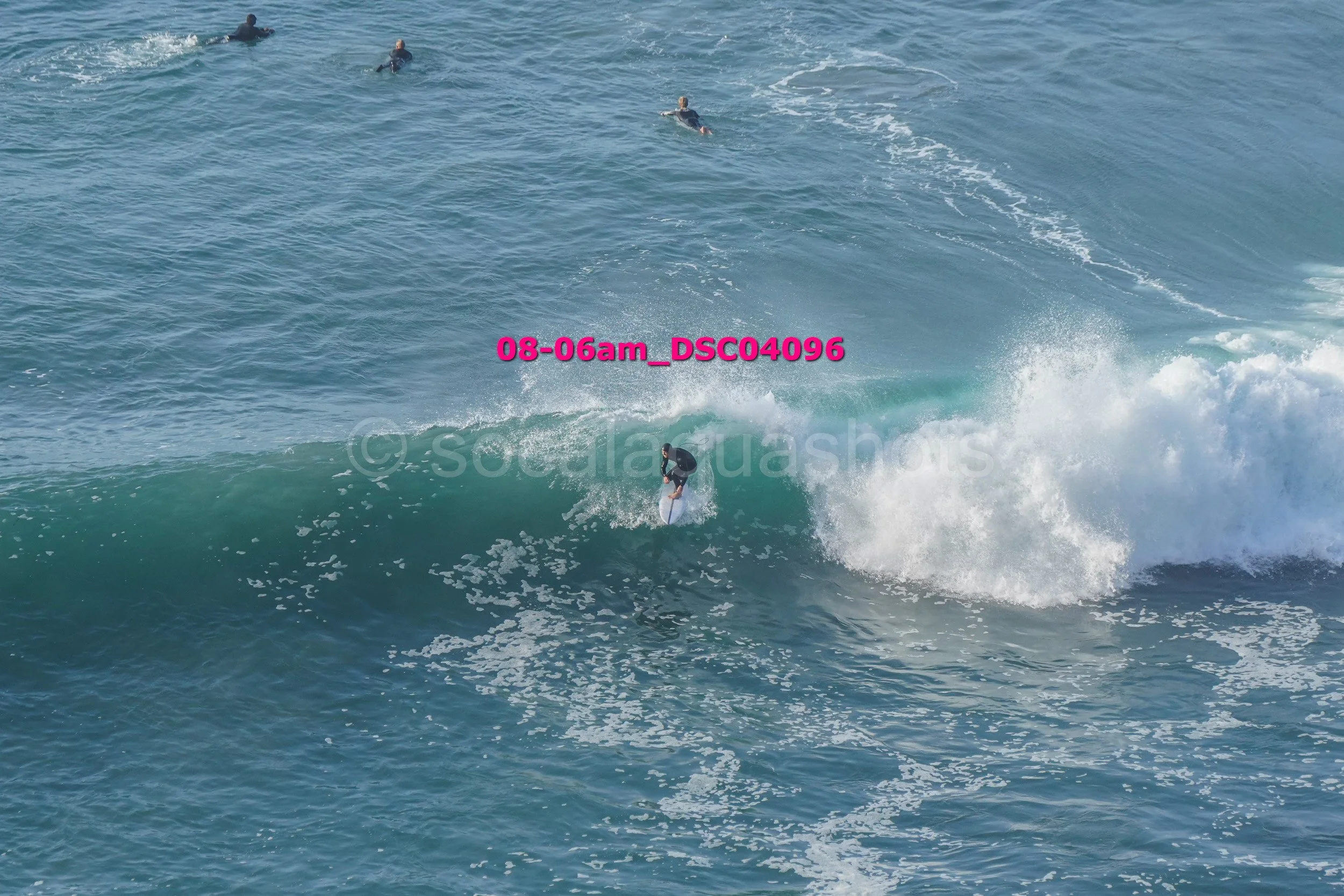 A surfer riding a wave with three other surfers visible in the ocean in the background.