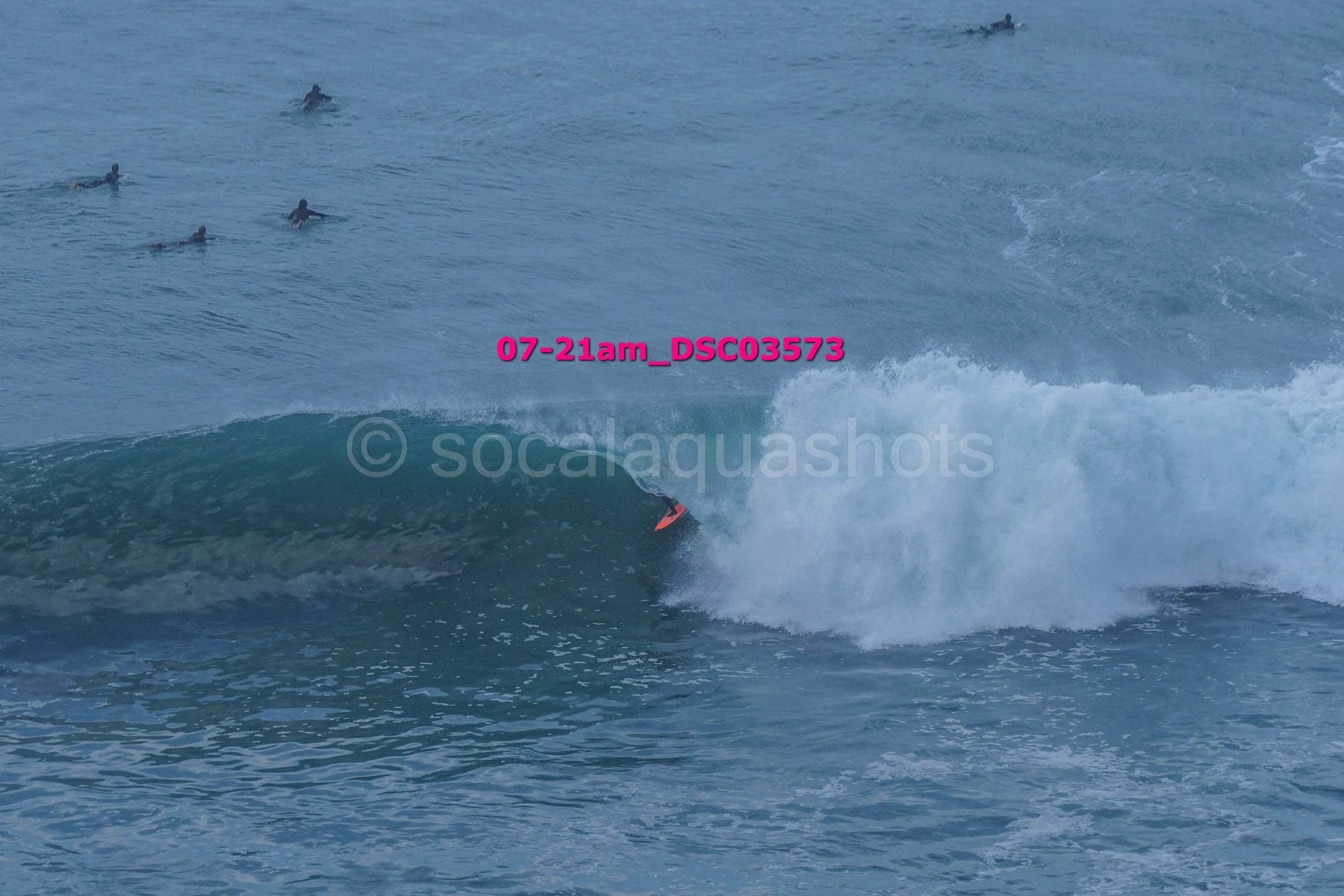 A person surfing on a wave in the ocean with several swimmers in the background.