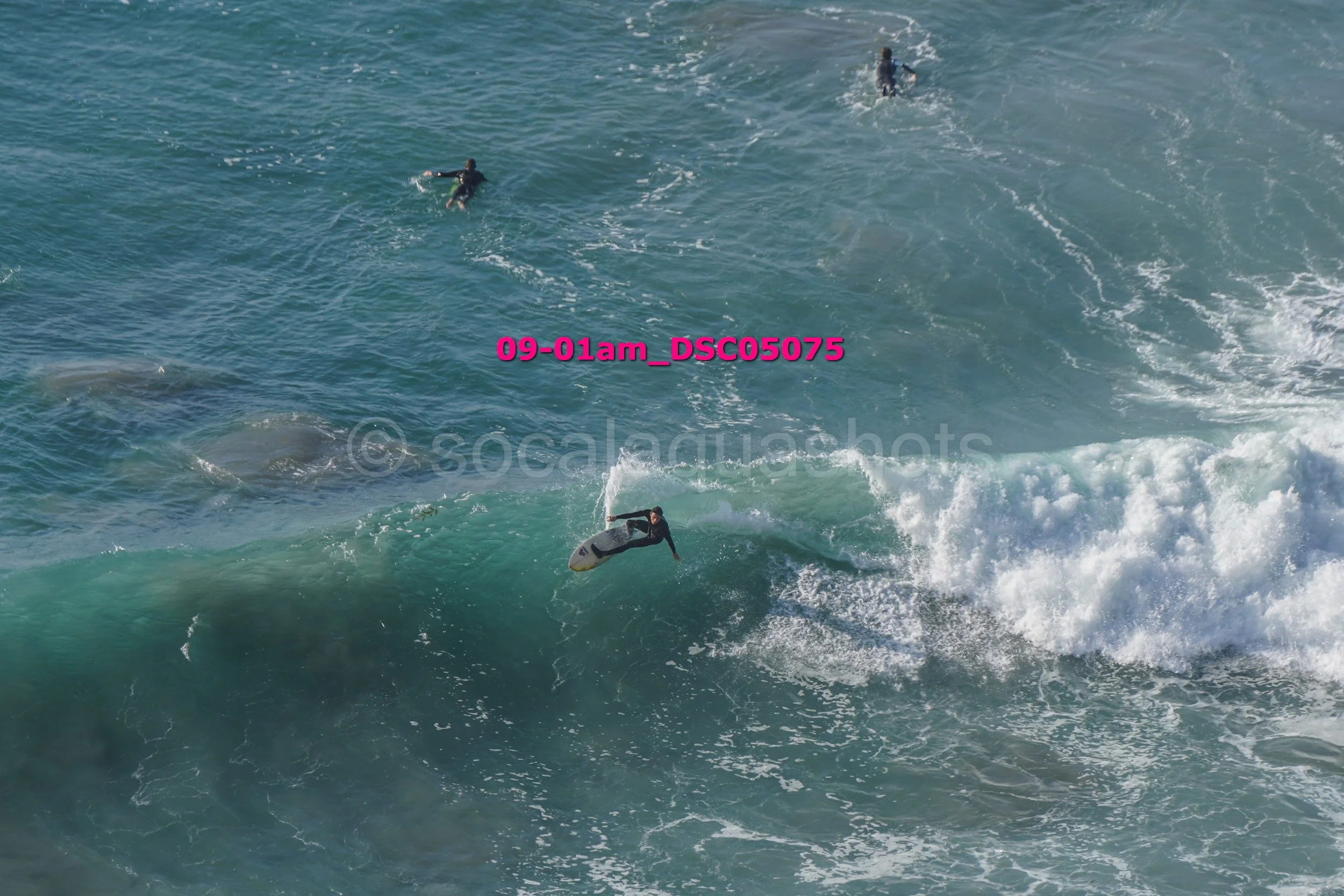 A surfer riding a wave while other surfers swim in the ocean nearby.