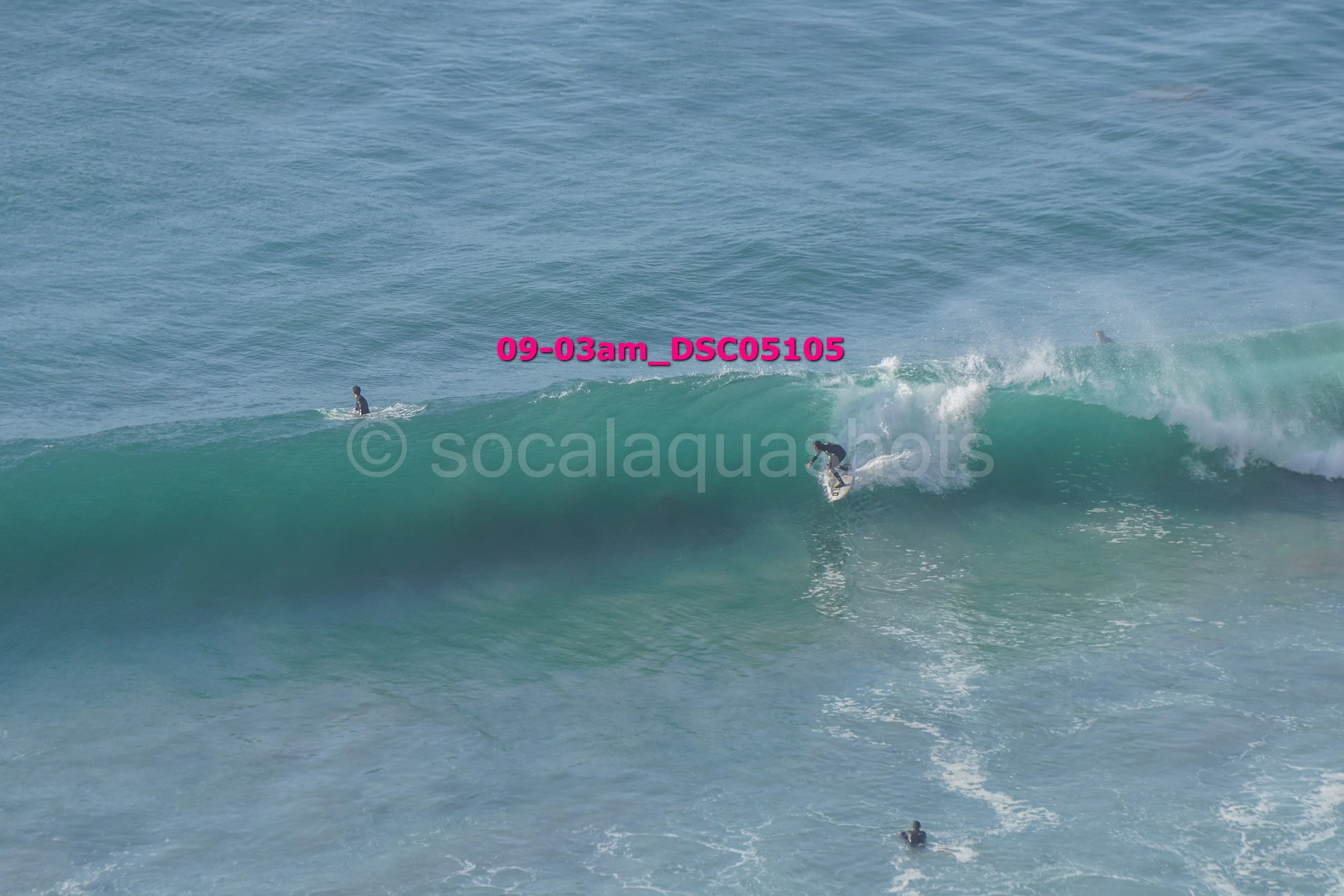 Surfer riding a large wave in the ocean with other surfers in the water nearby.