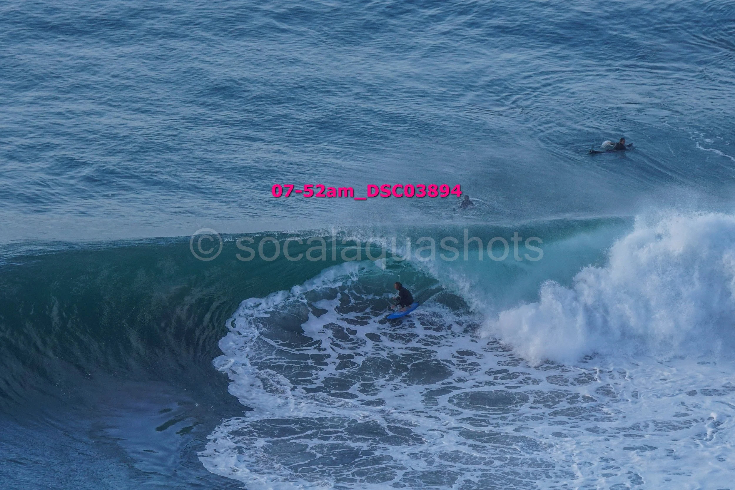 A surfer riding a wave with two other surfers visible in the background in the ocean.