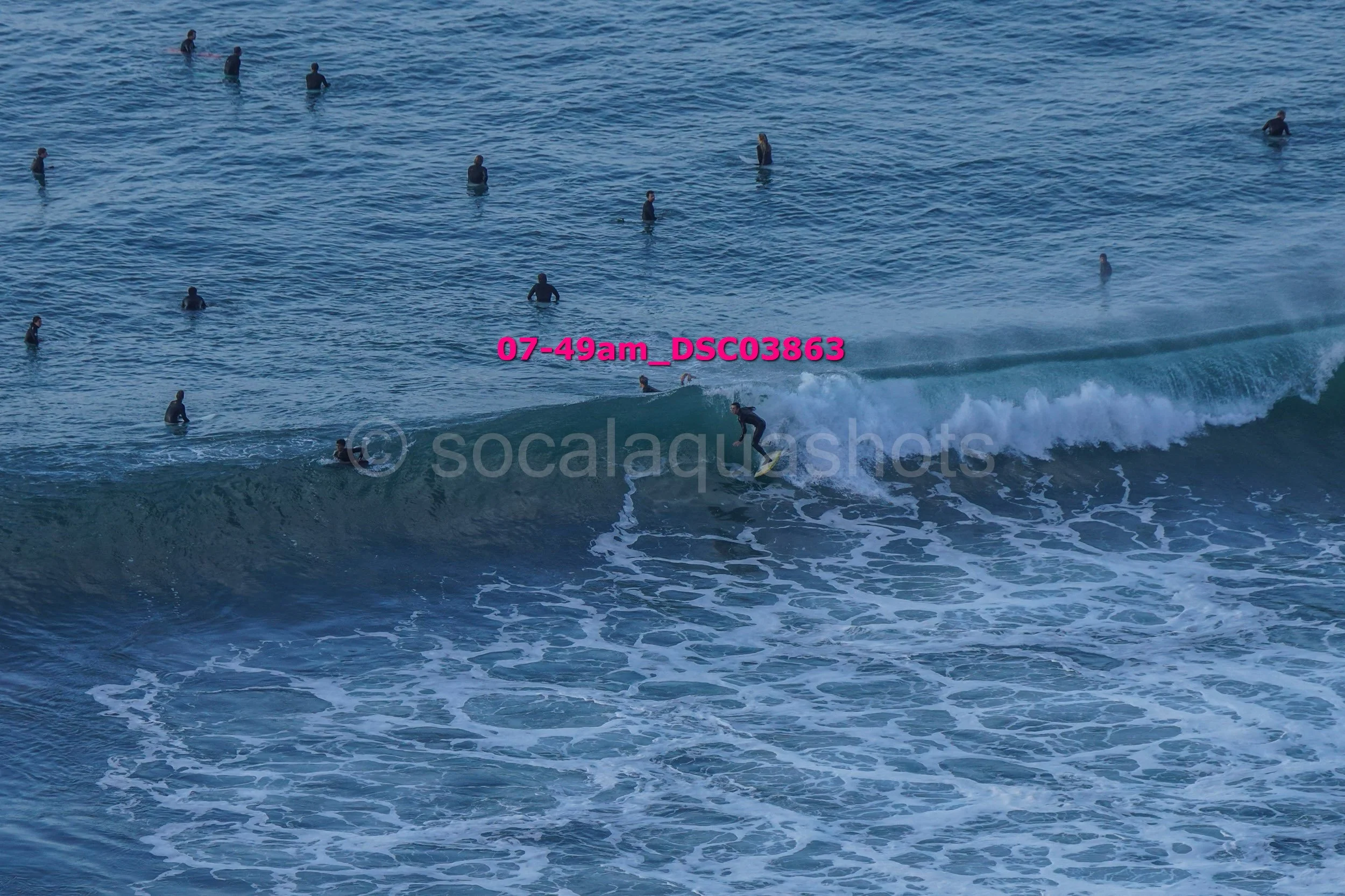 A person surfing on a wave near the shore while several people are swimming in the ocean.