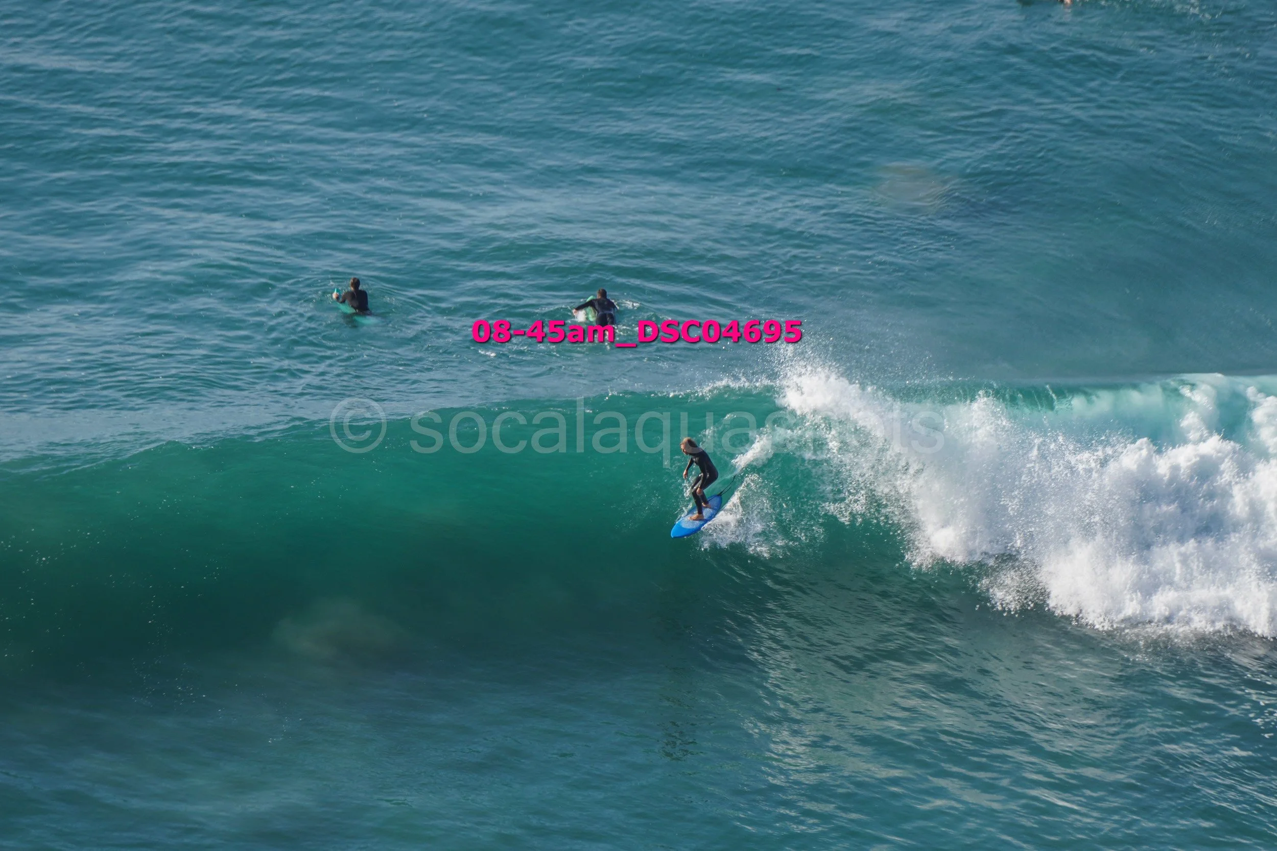 A surfer riding a wave while two other surfers are seen in the background in the ocean.