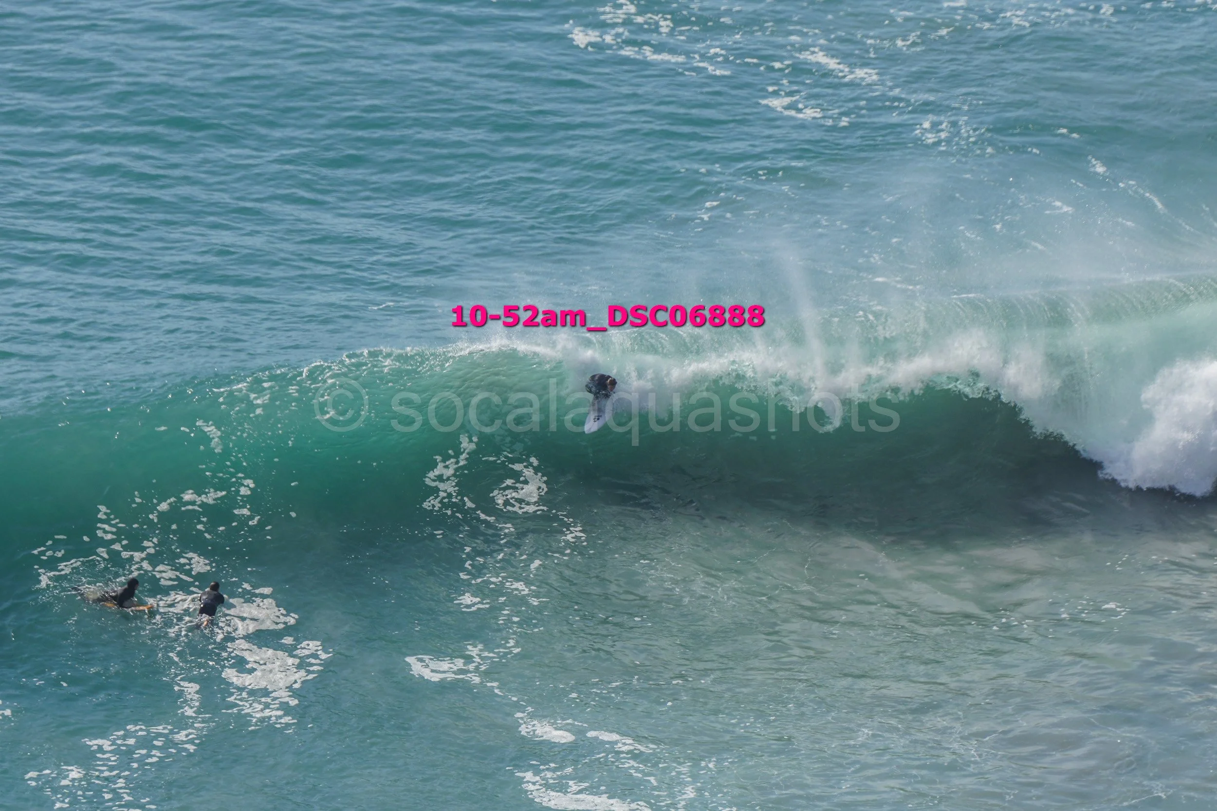 Surfer riding a large wave with two additional surfers in the water nearby.