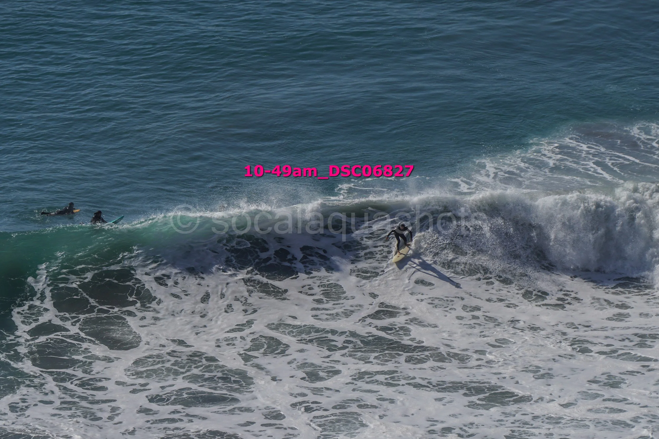 A surfer riding a wave with two other surfers paddling nearby in the ocean.
