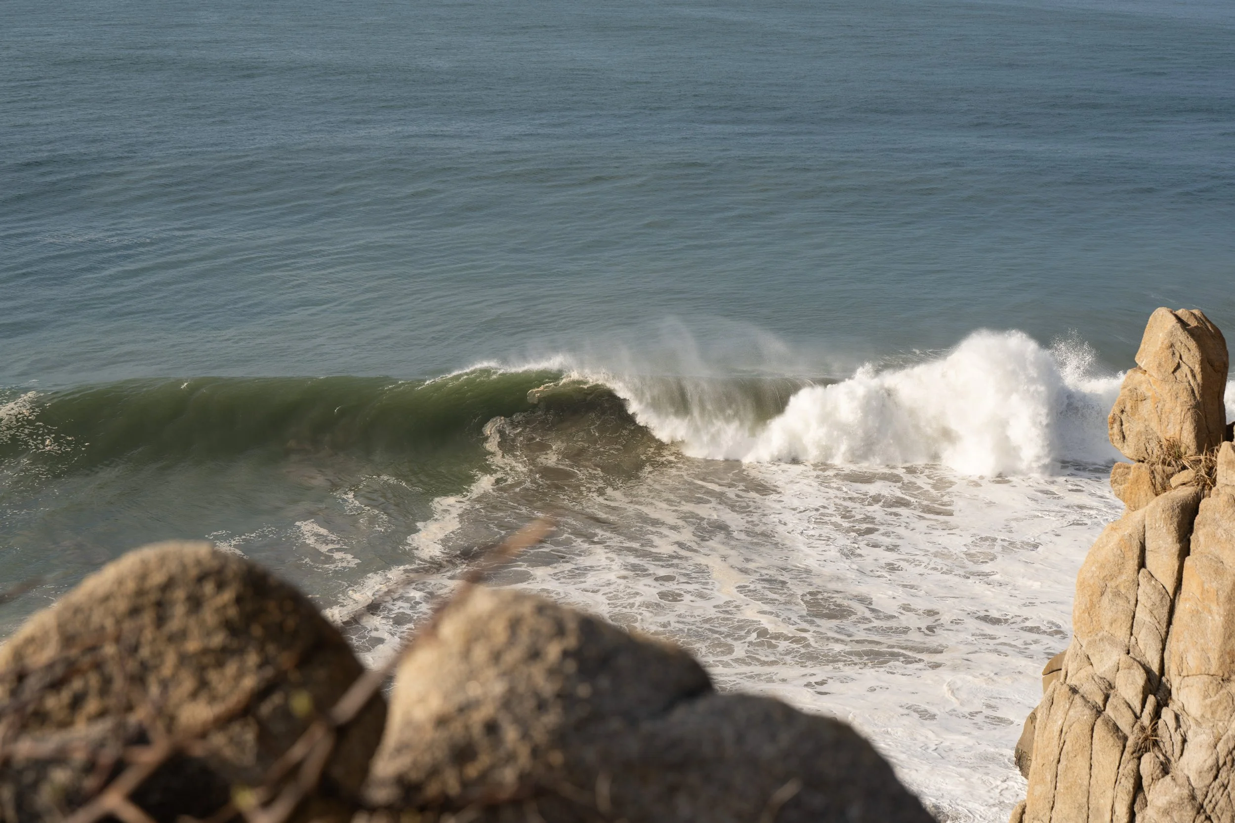 View of ocean waves crashing against rocks near the shore on a clear day.