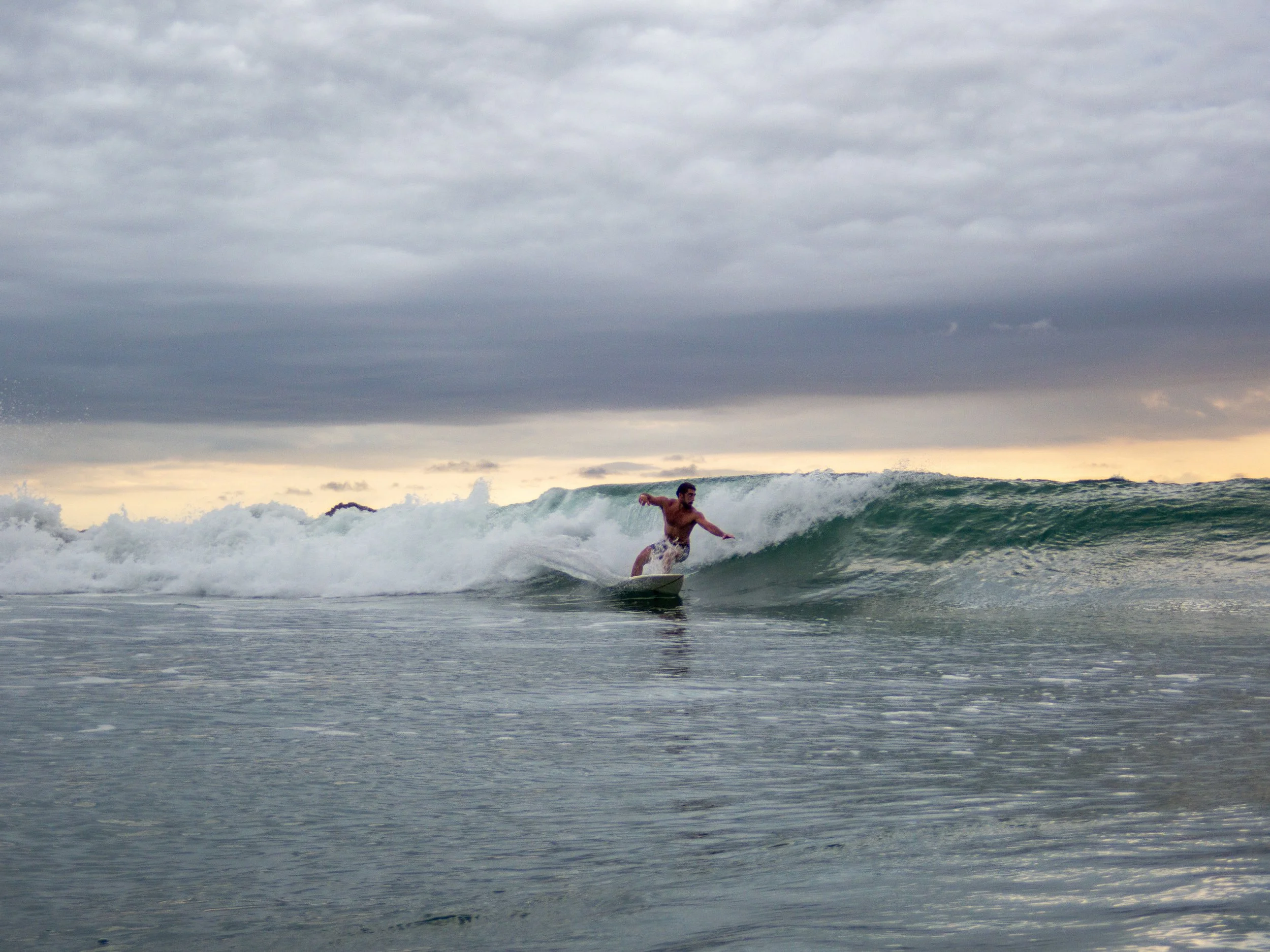 Surfer riding a wave during a cloudy sunset
