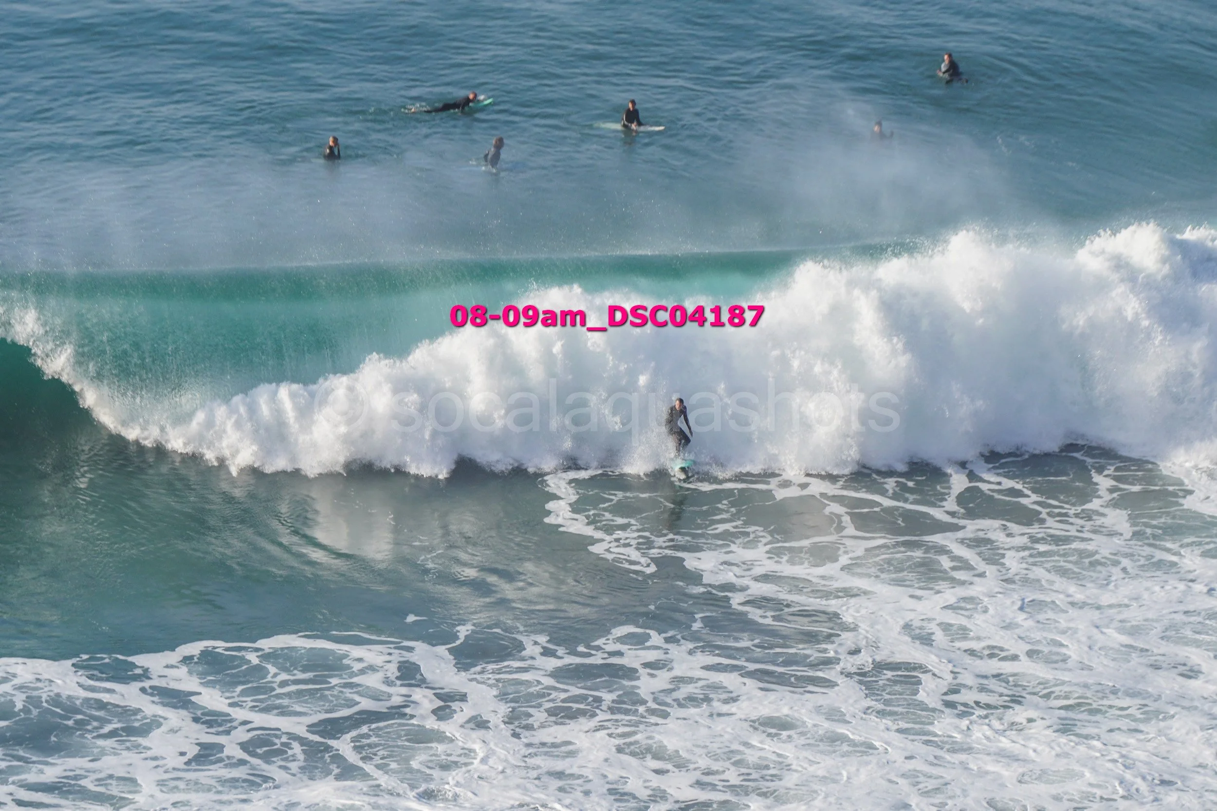 A person surfing on a large wave with smaller waves and other surfers in the background in the ocean.