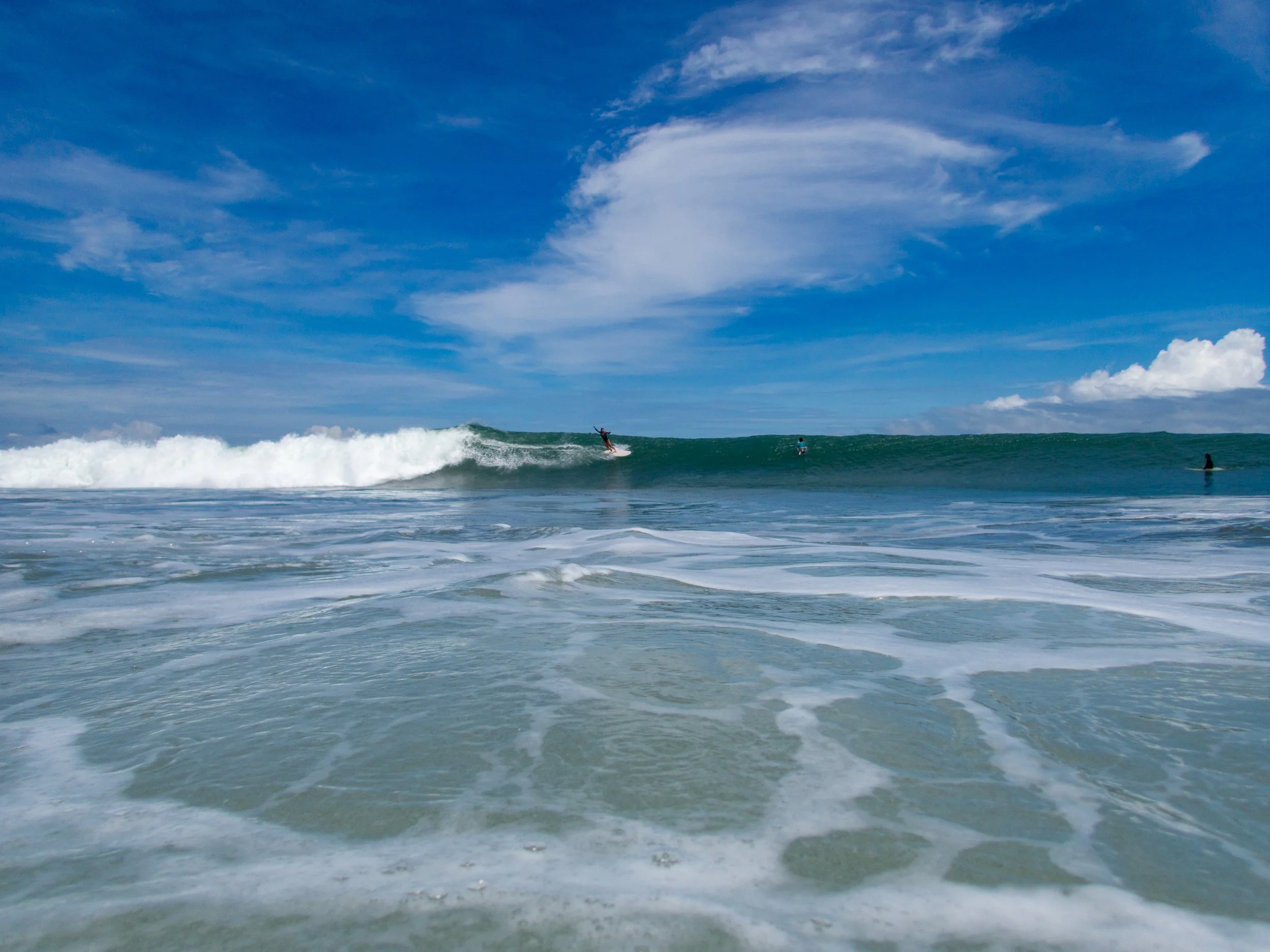 ocean waves with surfers under blue sky