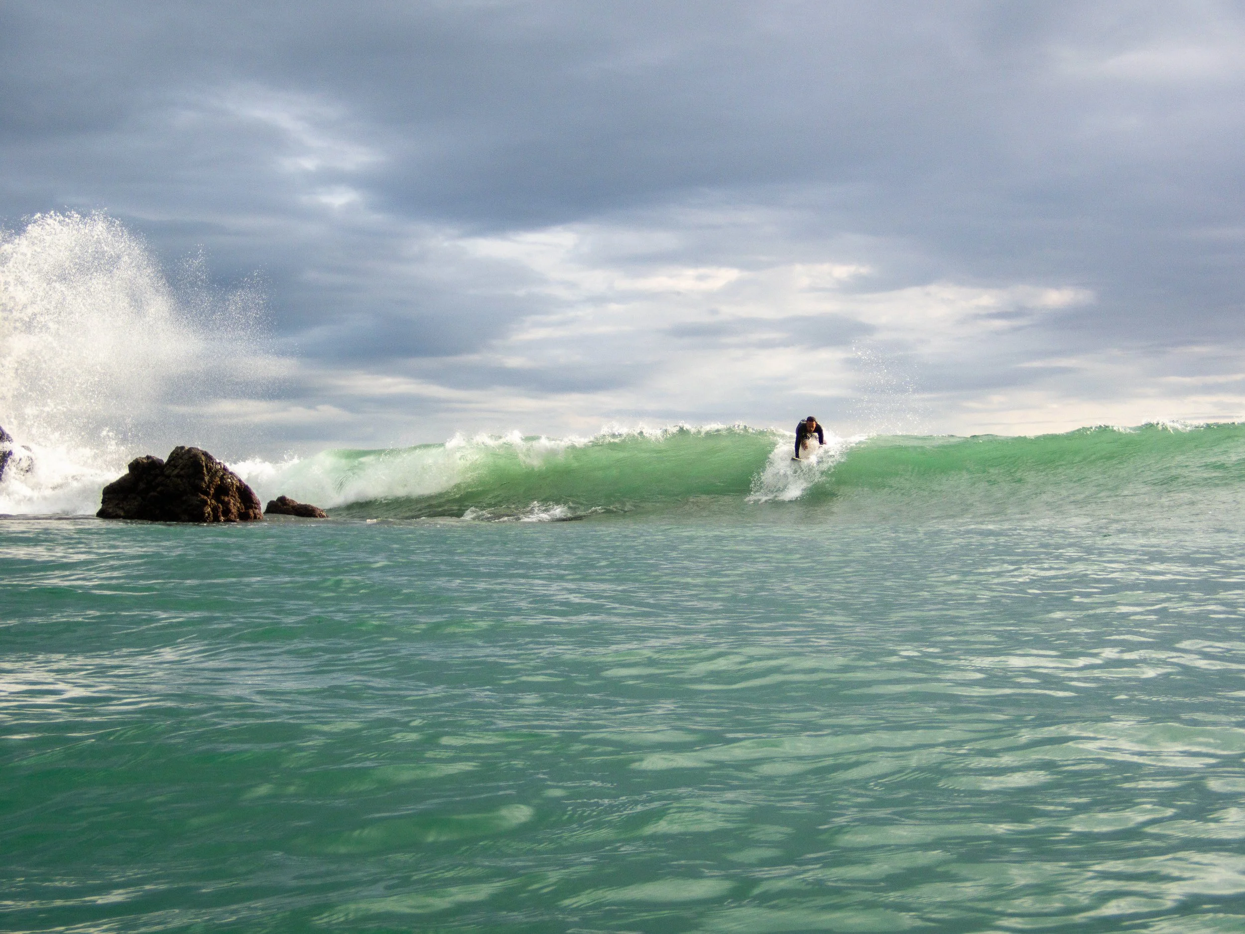 Surfer riding a wave near rocky shoreline under cloudy sky