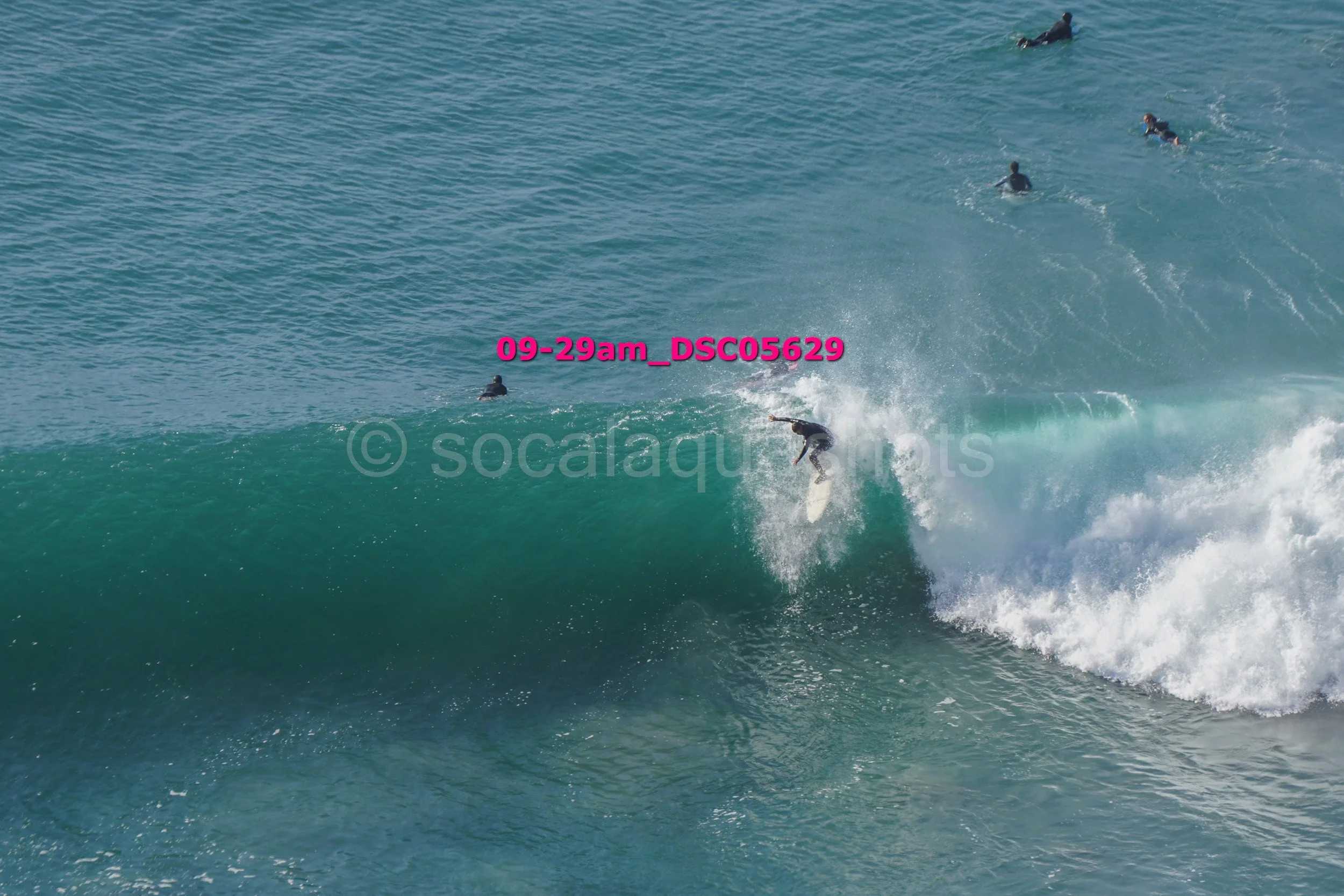 Surfer riding a wave with multiple surfers in the water nearby, captured at 9:29 am.