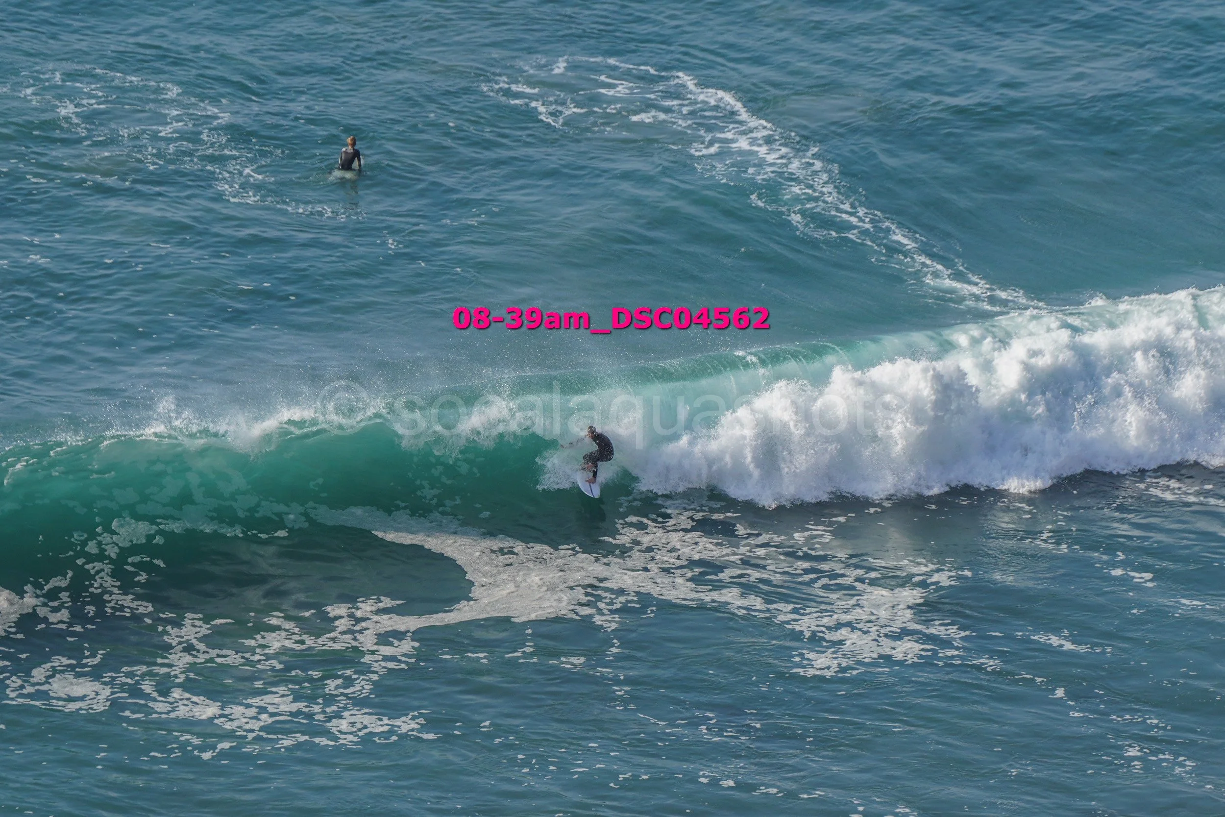 Person surfing on a wave in the ocean with another person swimming in the background.