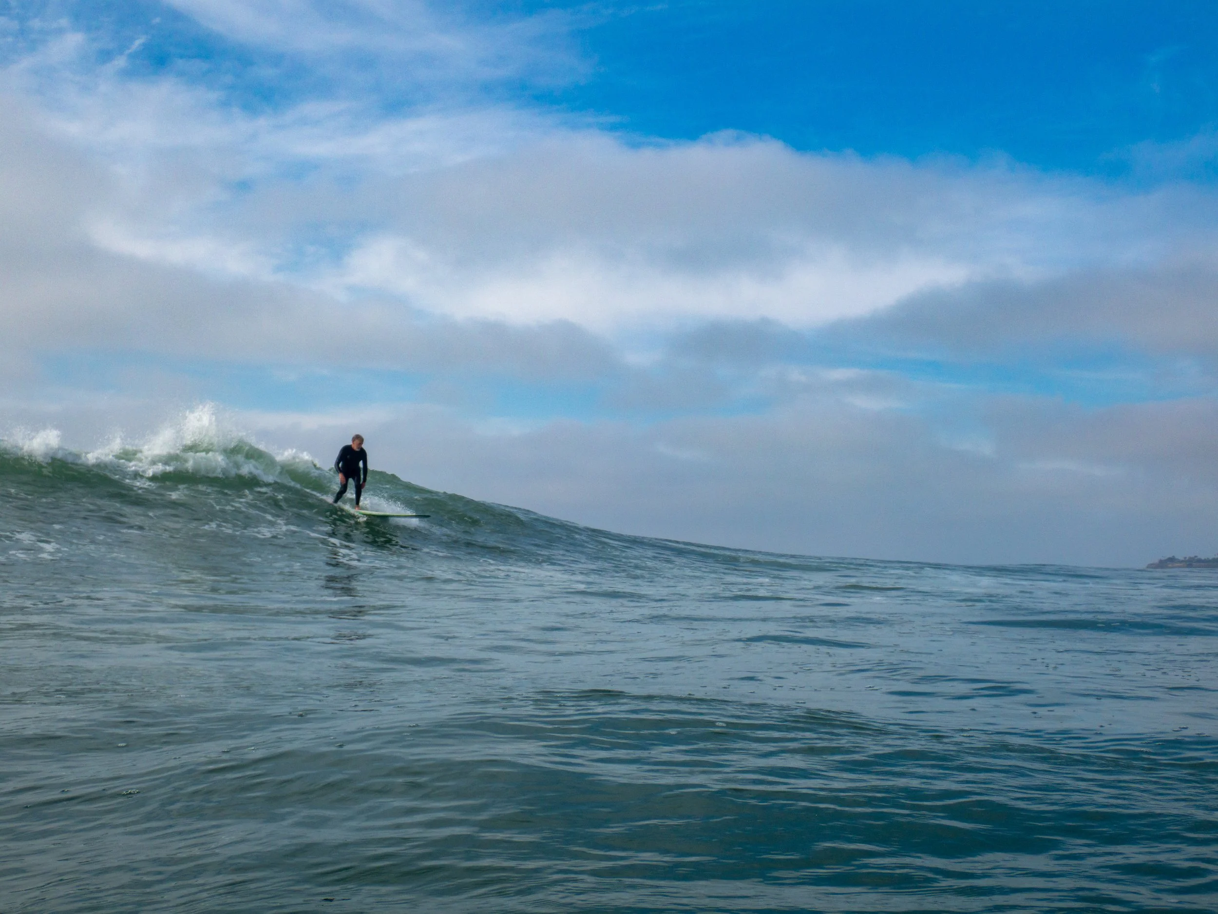 A person surfing on a small wave under a partly cloudy sky in the ocean.