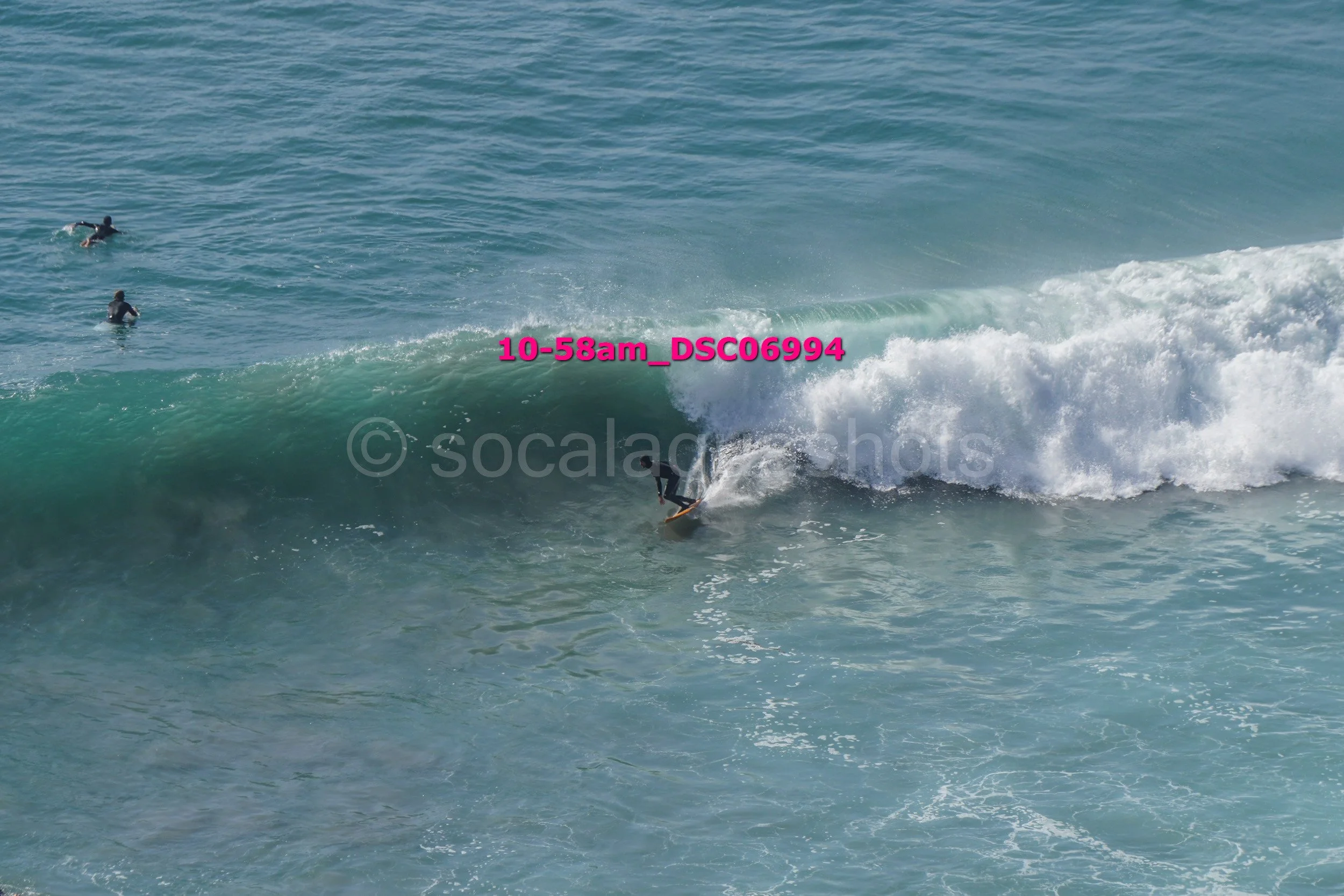 A surfer riding a wave while two other surfers are in the water nearby.