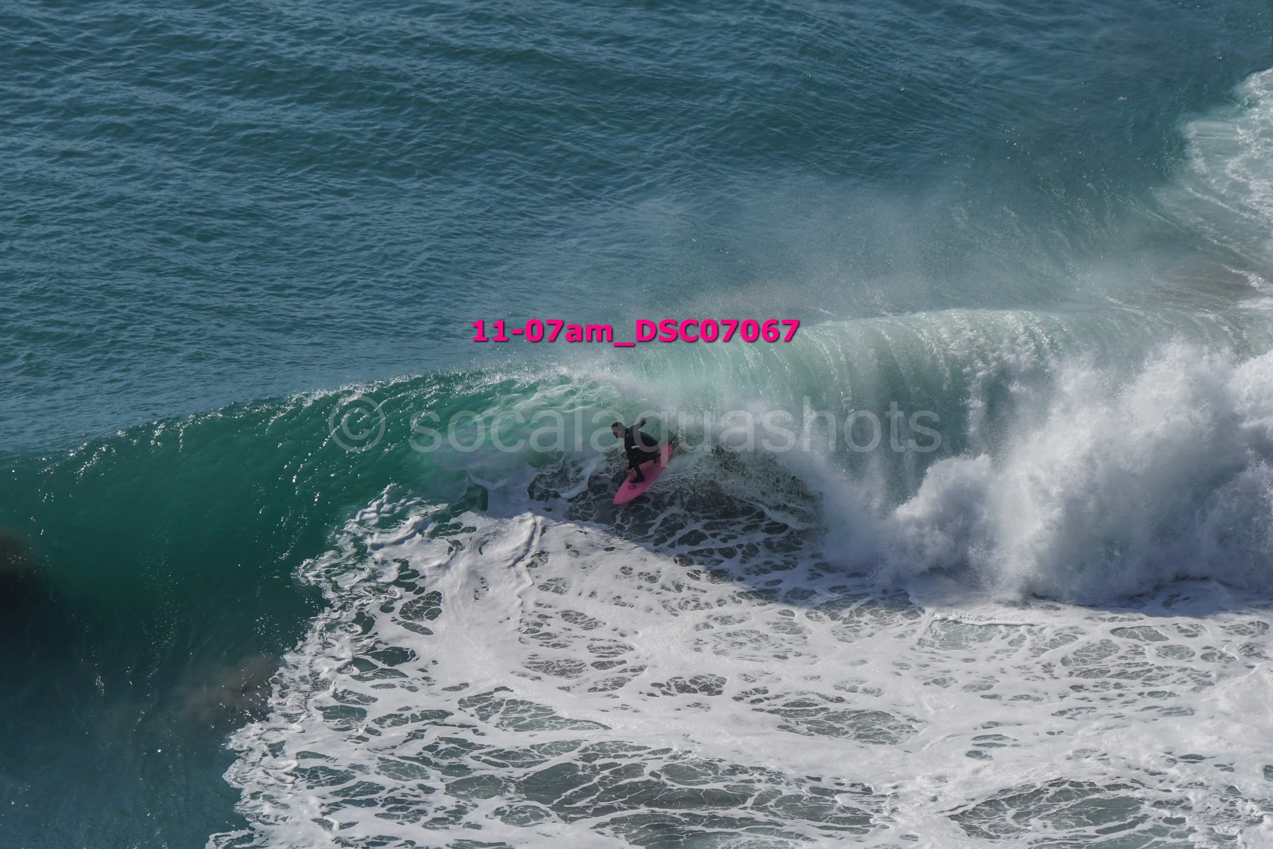 A person surfing on a pink surfboard riding a large ocean wave.