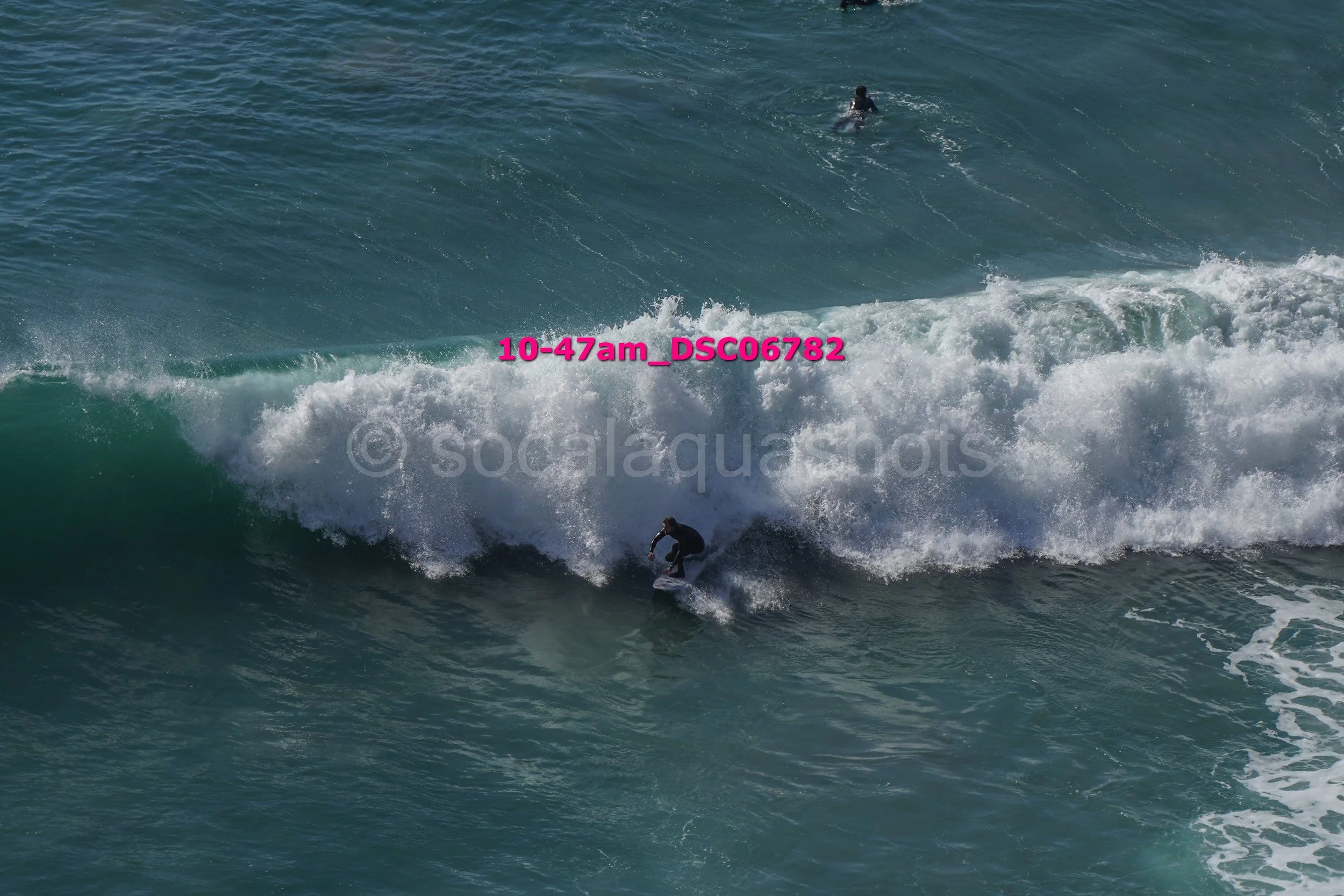 A person surfing on a wave in the ocean, with another surfer in the background.