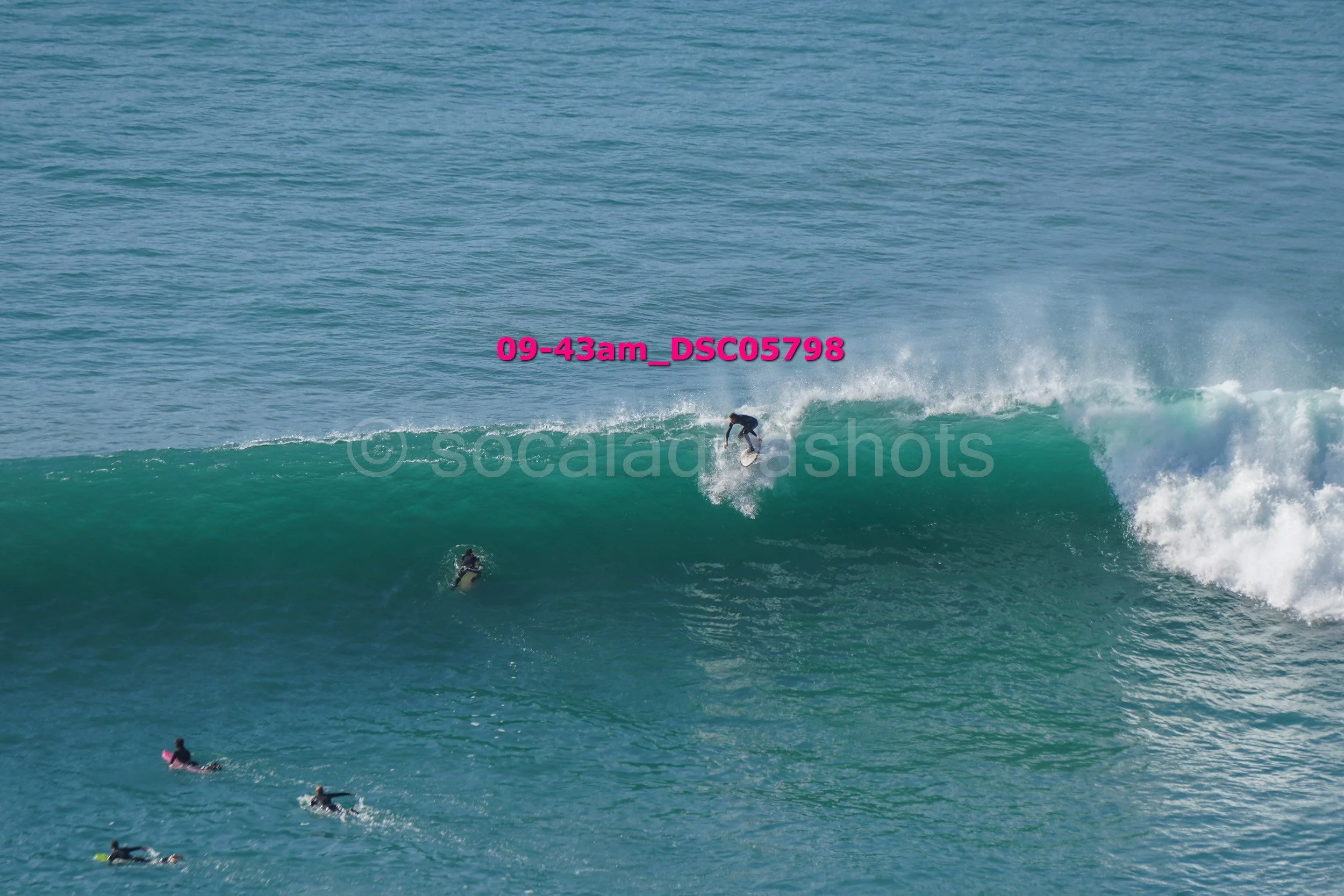 Surfer riding a wave in the ocean with several other surfers paddling nearby