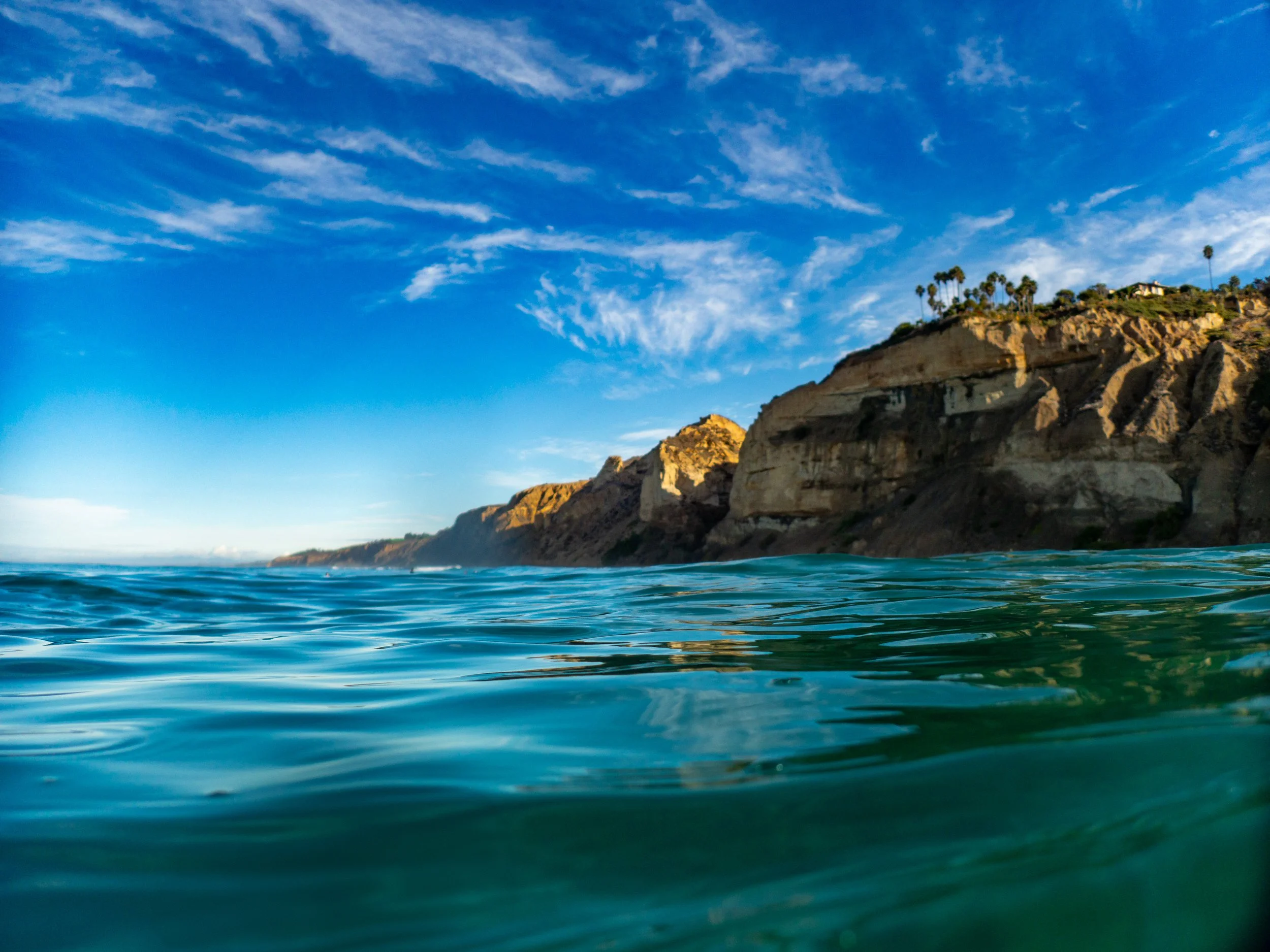 Ocean water with cliffs and palm trees on a sunny day with blue sky and clouds.