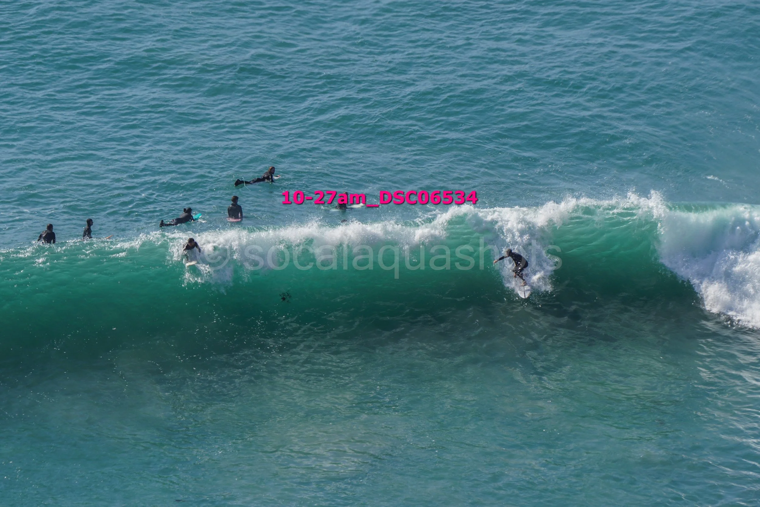 Several people surfing in ocean waves, with one person actively riding a wave on a surfboard.
