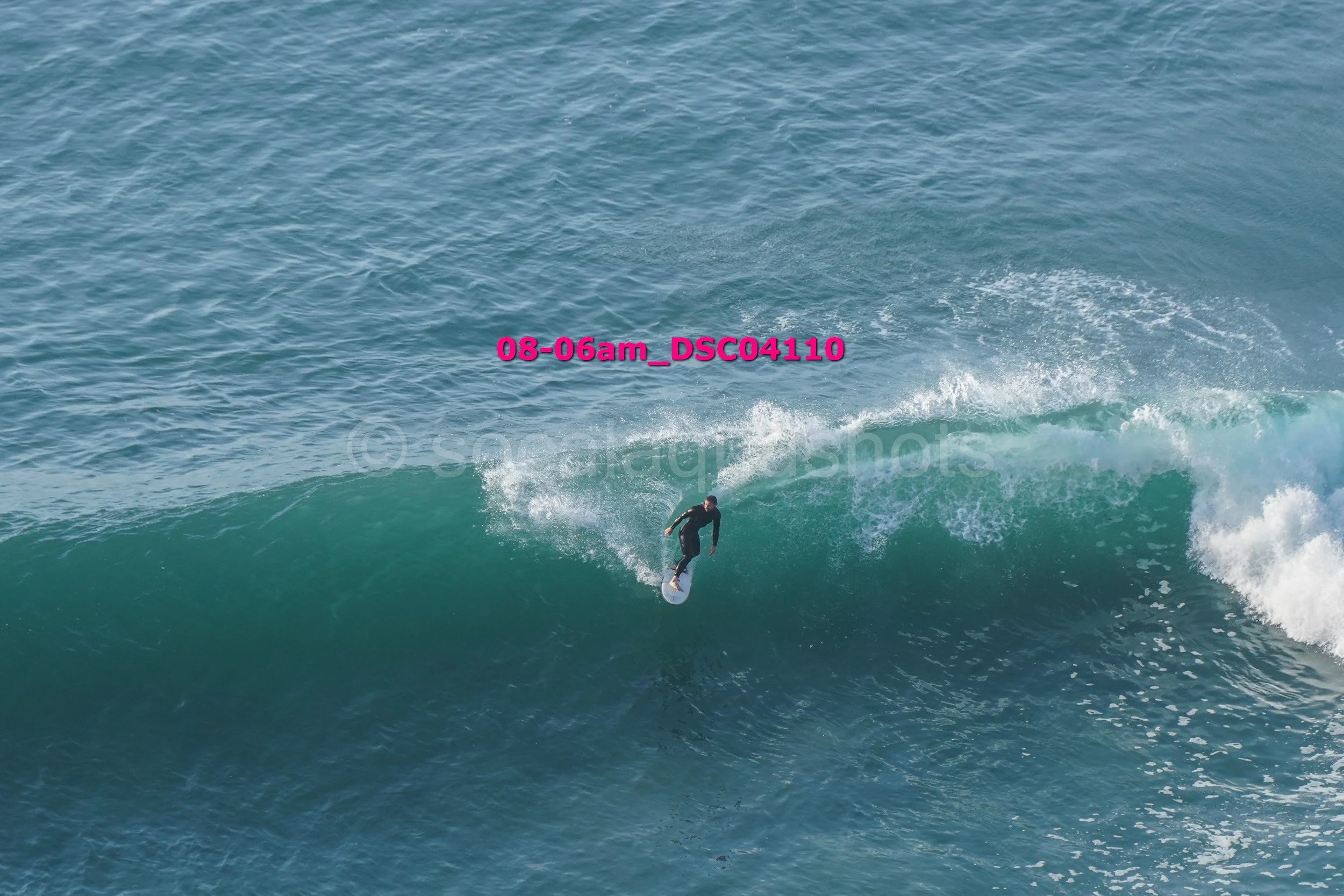 A person surfing on a large wave in the ocean, wearing dark clothing and riding a surfboard.