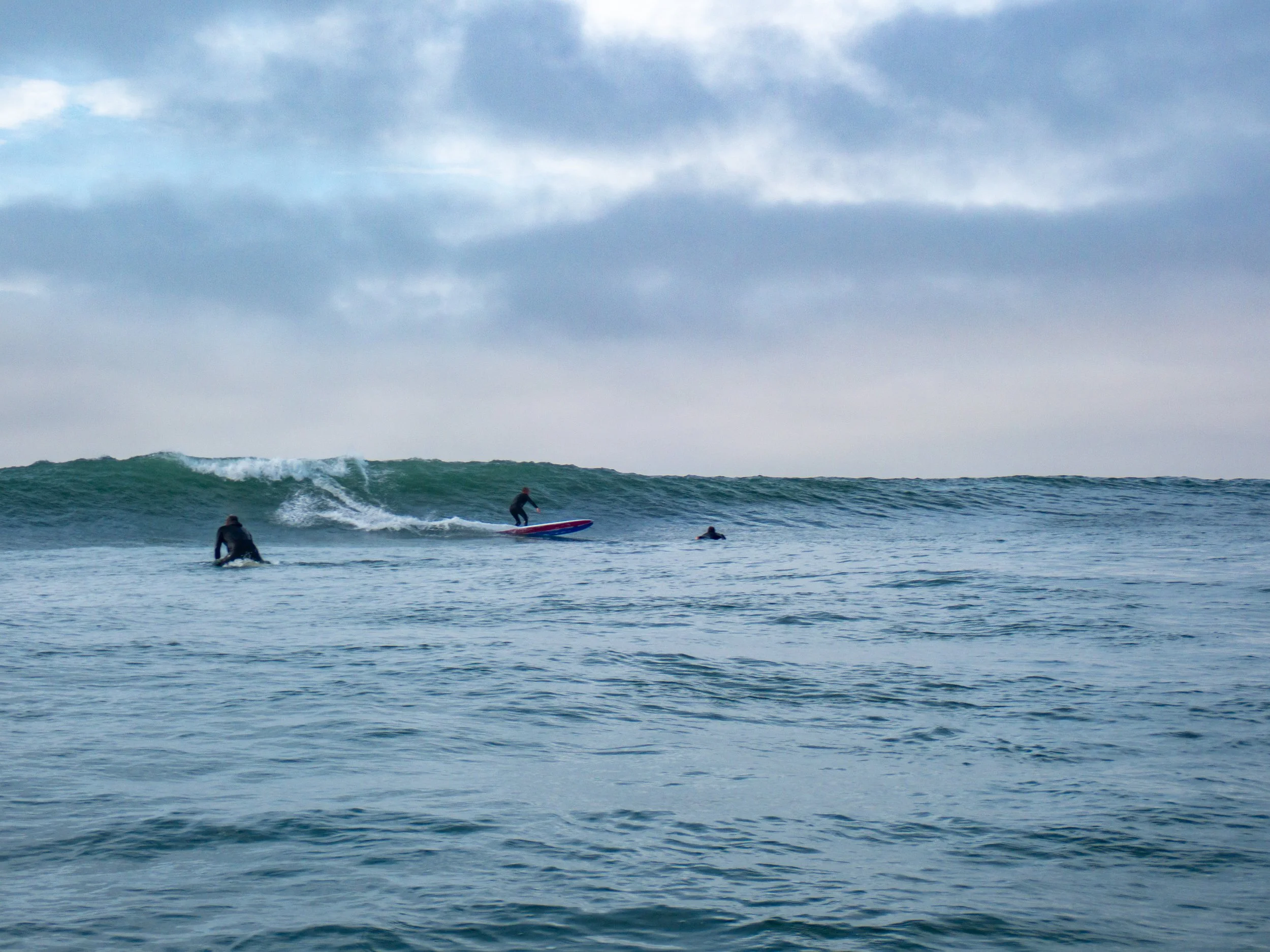 People surfing on ocean waves under cloudy sky.
